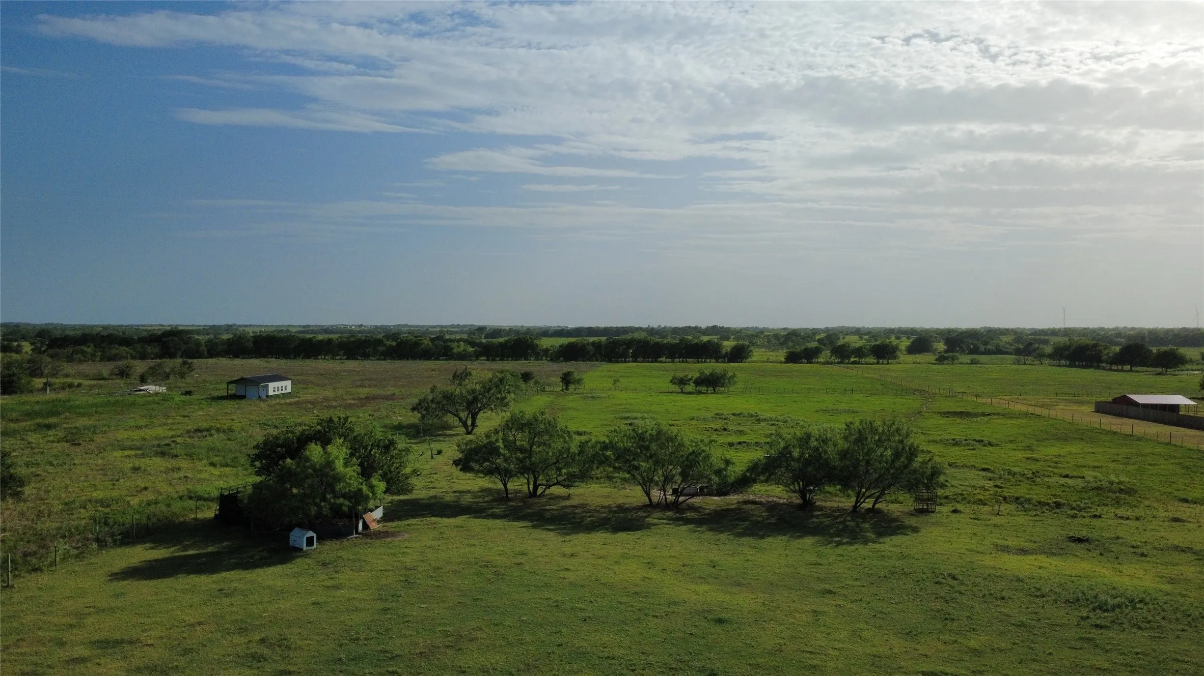 Expansive green acreage with scattered mature trees and distant structures