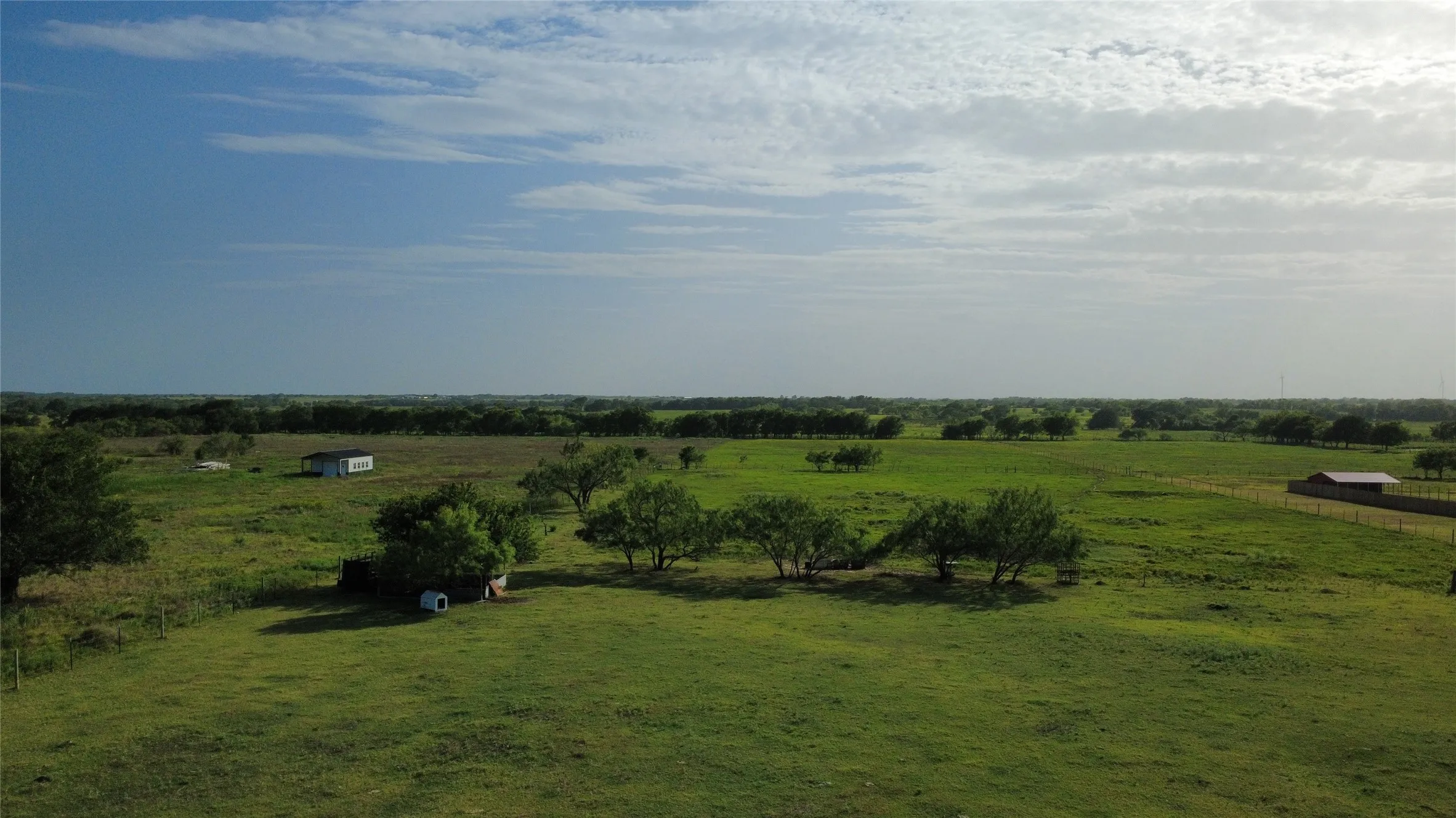 Sprawling pastoral acreage featuring lush green pastureland, mature shade trees, and scattered outbuildings