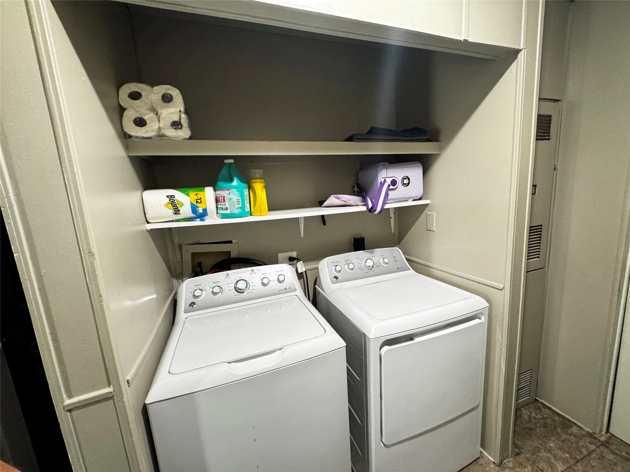 Built-in shelving, white washer, white dryer, wall paneling, and vinyl flooring