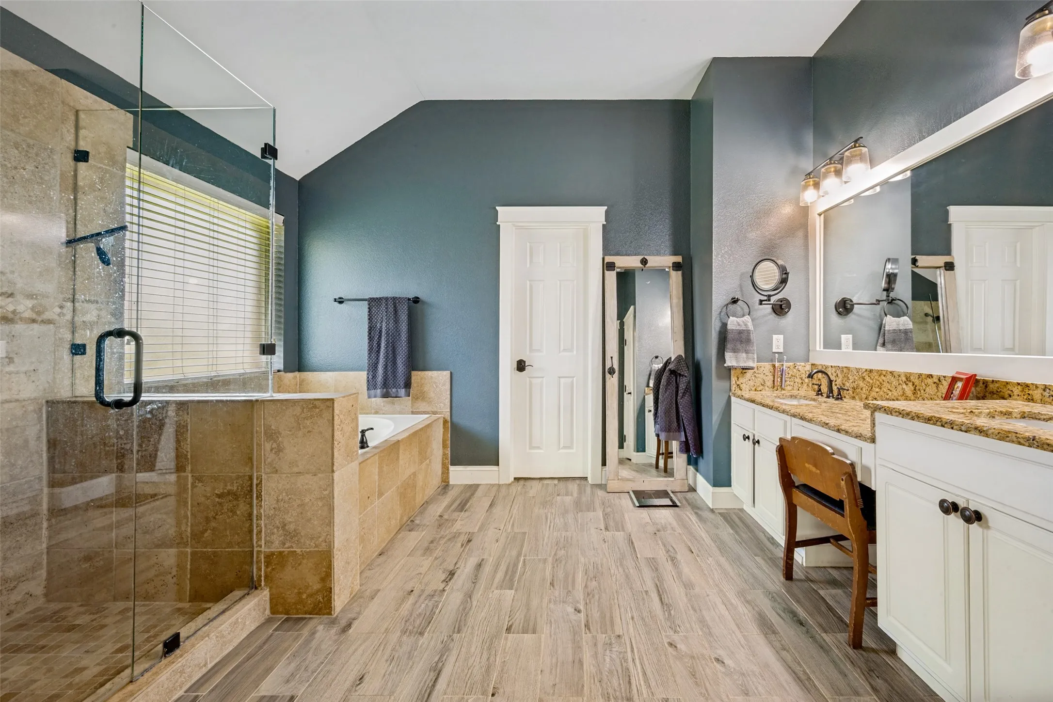 Spacious bathroom featuring a glass-enclosed shower, a separate soaking tub with tiled surround, and wood-finish flooring