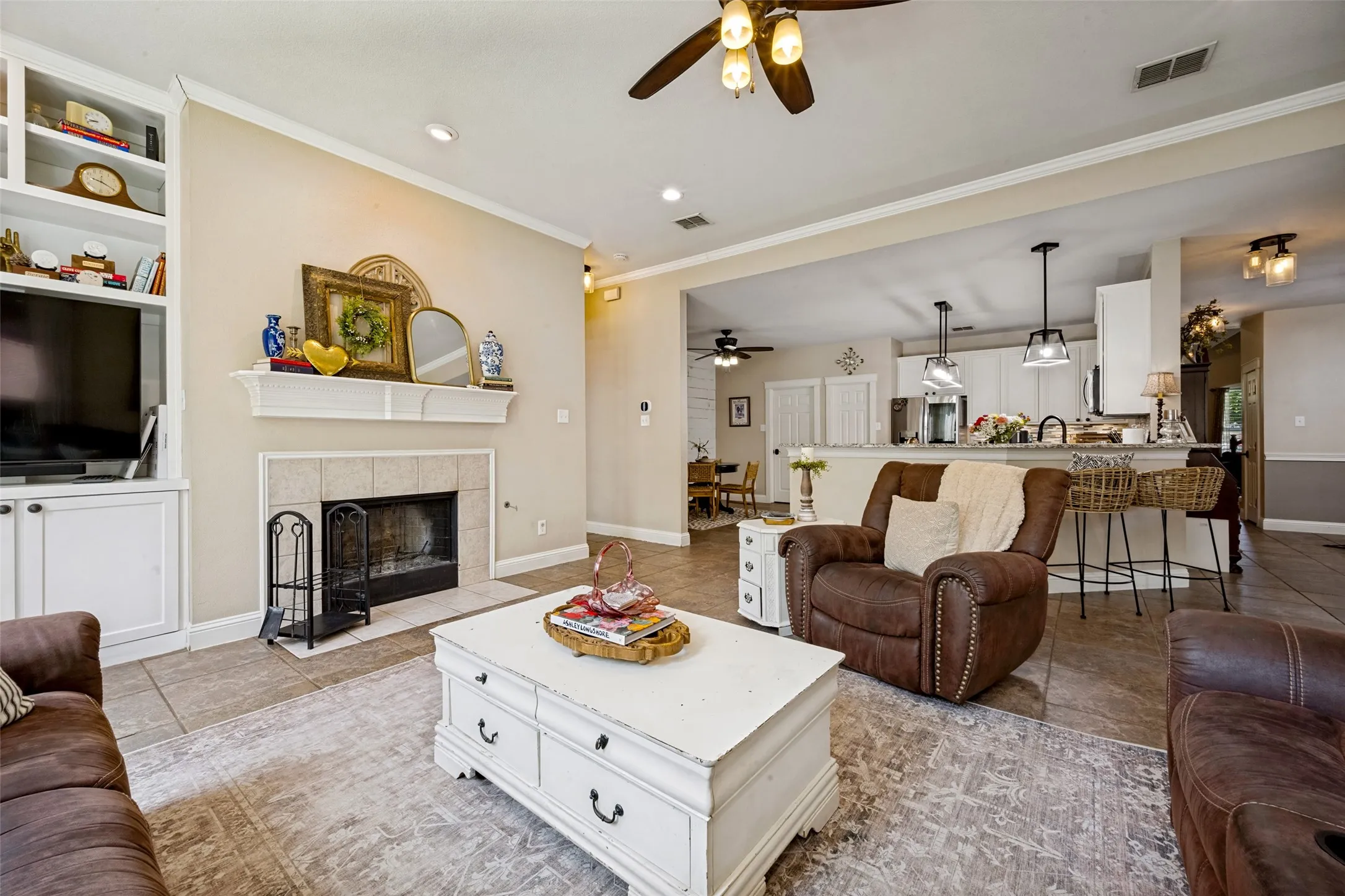 Living area featuring a fireplace with a tiled surround, built-in cabinetry, crown molding, a ceiling fan, and tile flooring