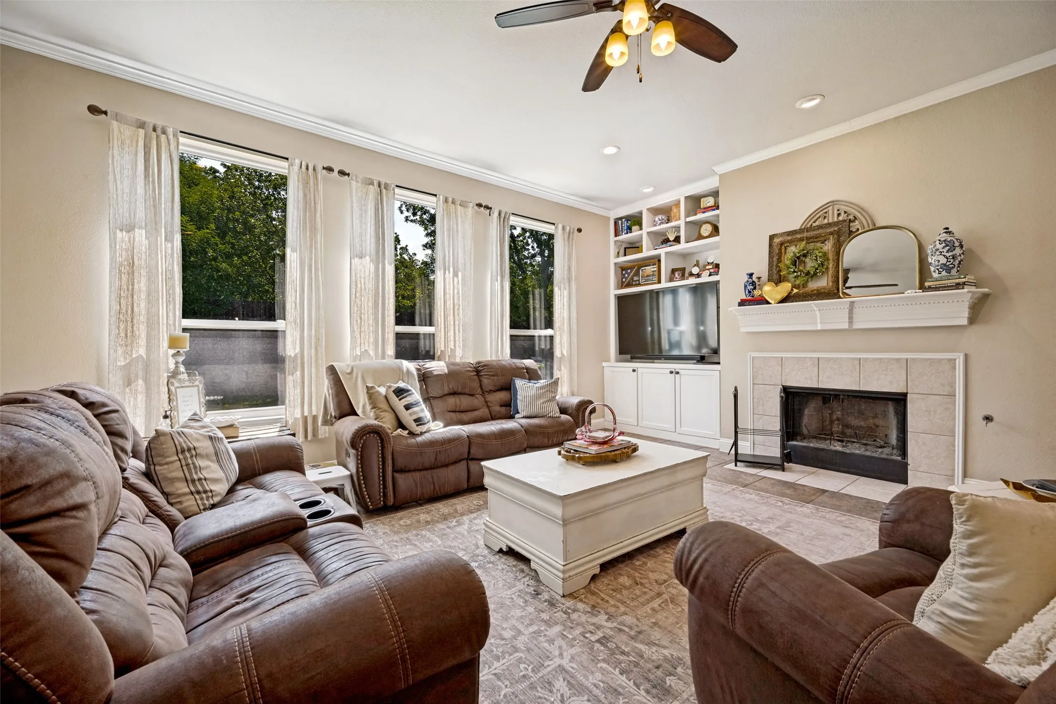 Living area featuring a fireplace with a tile surround and mantle, built-in shelving and cabinetry, recessed lighting, and a ceiling fan