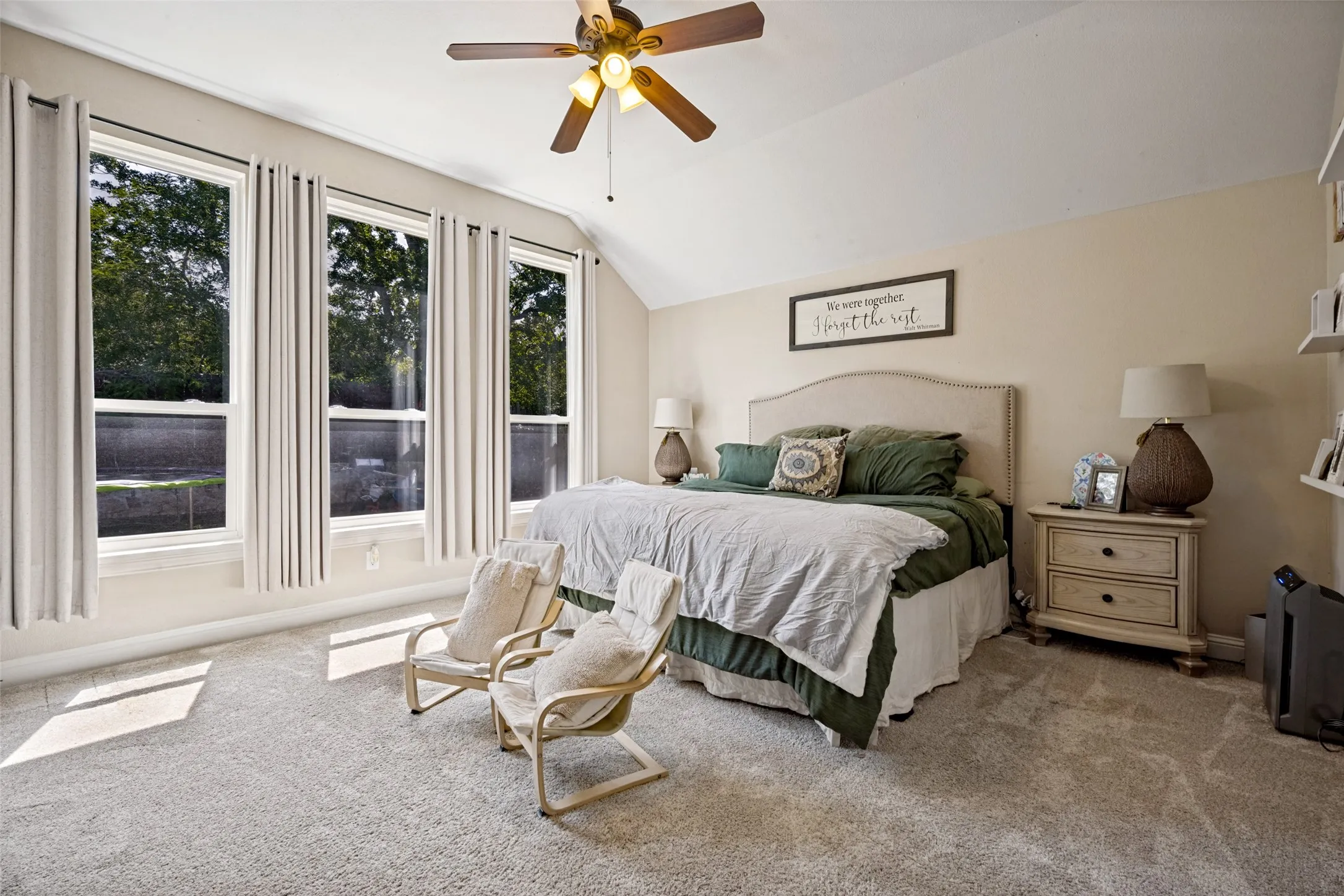 Expansive bedroom featuring vaulted ceilings, a ceiling fan with integrated lighting, and three tall windows