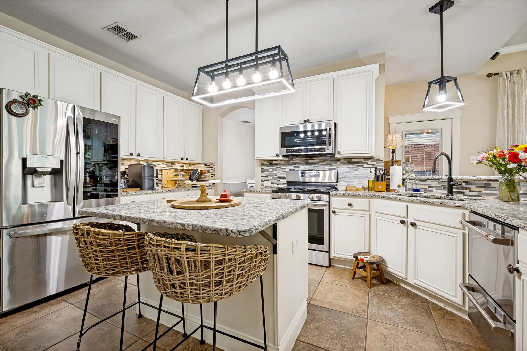 Bright kitchen featuring white cabinetry, granite-finish countertops, stainless steel appliances, a multi-tone tile backsplash, and tile flooring