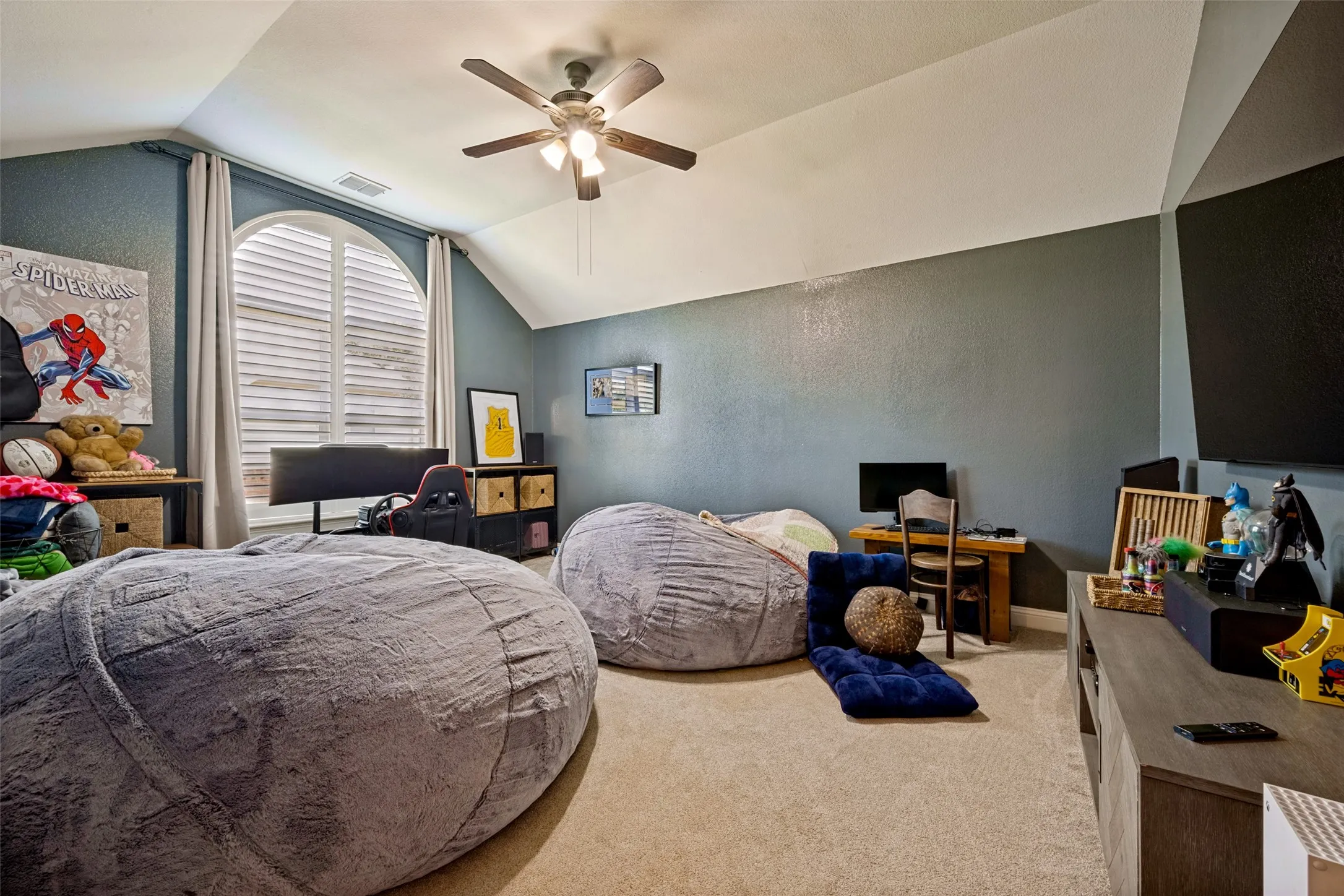 Spacious room featuring vaulted ceilings, a ceiling fan with integrated lighting, and a large arched window with horizontal blinds