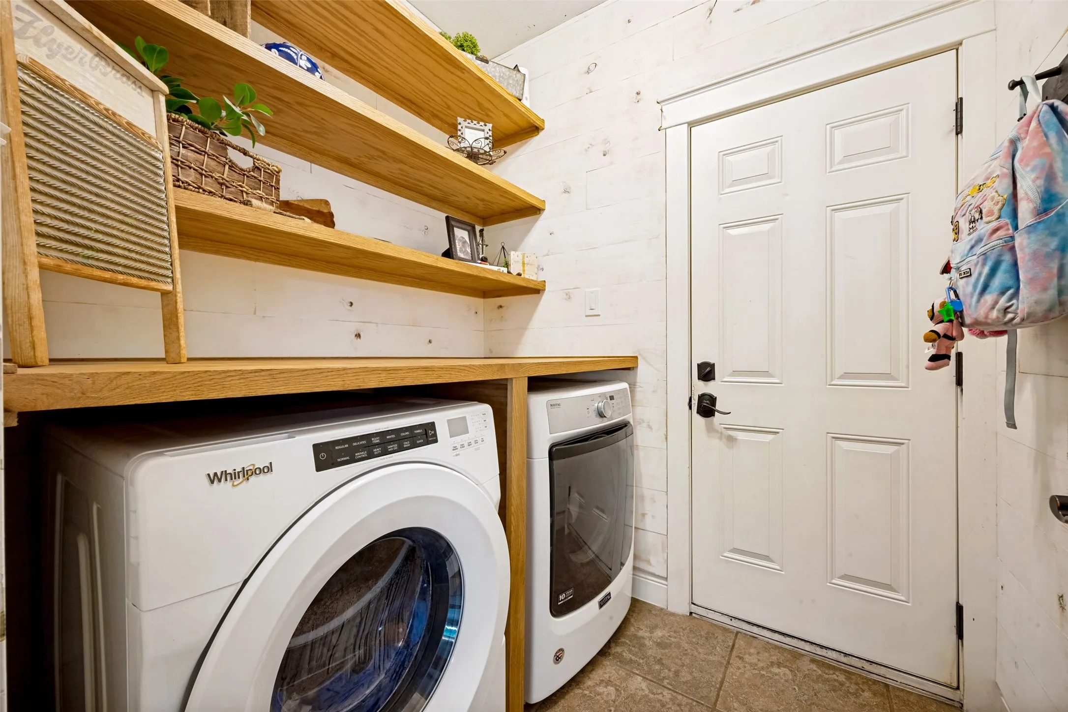 Laundry area with built-in wood-finish shelving, shiplap-style wall paneling, and tile flooring