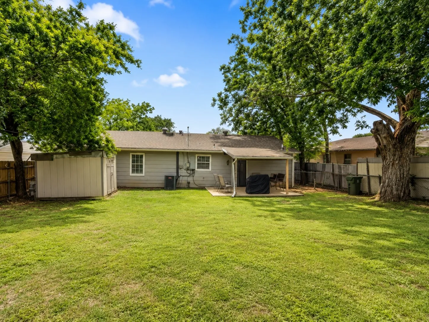 Expansive backyard featuring a covered patio, mature trees, a storage shed, and a privacy fence
