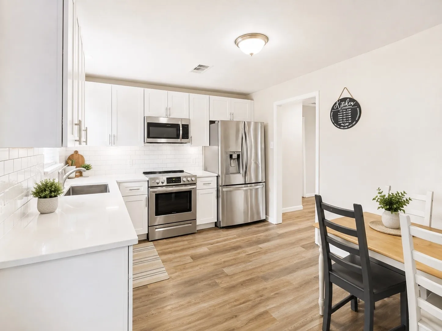 White shaker-style cabinetry with stainless steel hardware, white subway tile backsplash, stainless steel appliances, white countertops, and wood-finish flooring