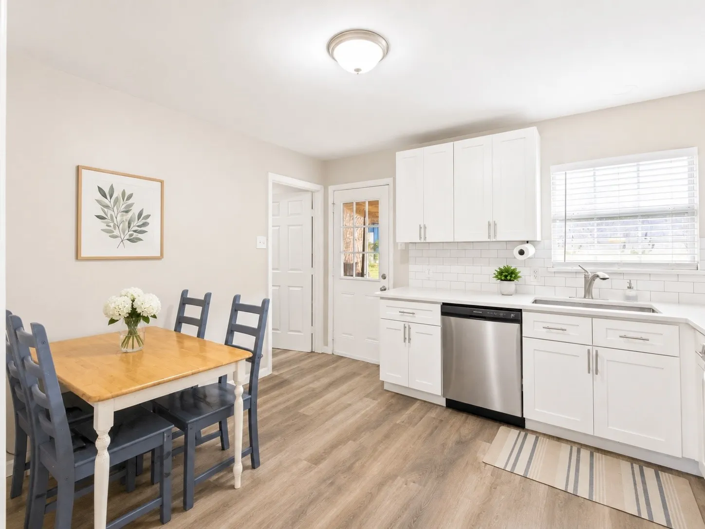 White shaker cabinetry, subway tile backsplash, stainless steel dishwasher, wood-finish flooring, and a single basin sink with a gooseneck faucet