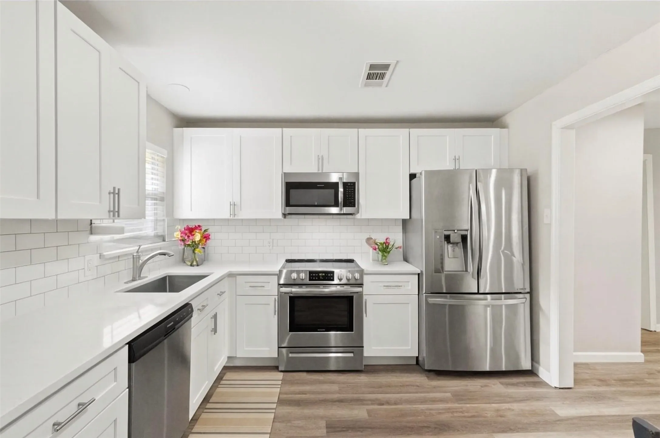 White shaker cabinetry, stainless steel appliances, white subway tile backsplash, white countertops, and wood-finish flooring