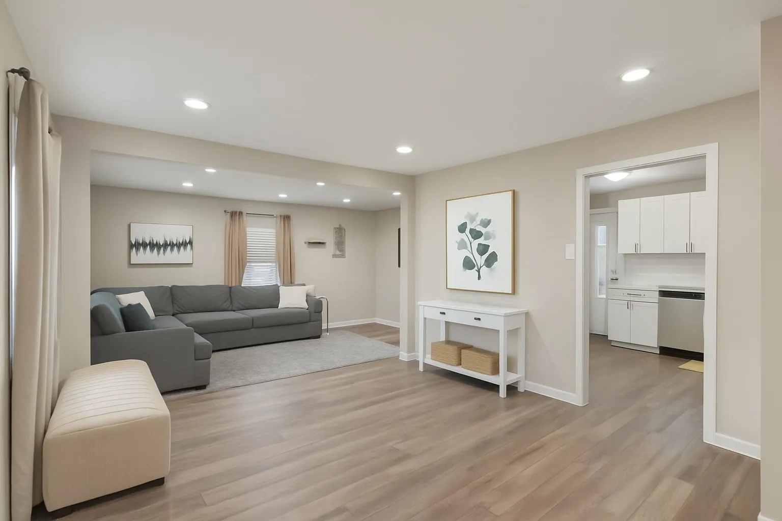 Recessed lighting, wood-finish flooring, neutral paint palette, and an open entryway to the kitchen featuring white cabinetry and stainless steel appliances