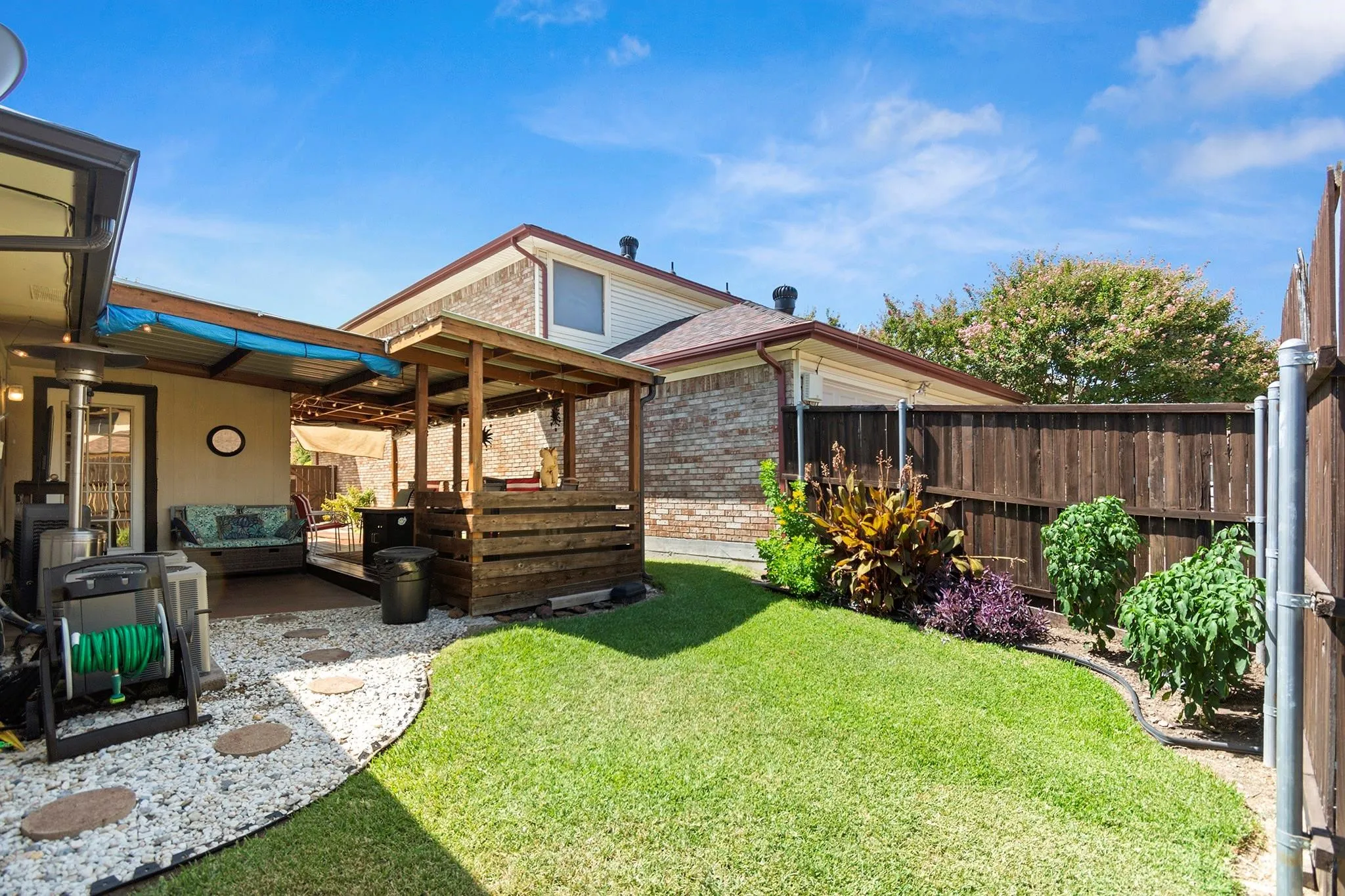 Landscaped backyard featuring a covered patio, a wooden pergola, a manicured lawn, a gravel patio with stepping stones, and a privacy fence