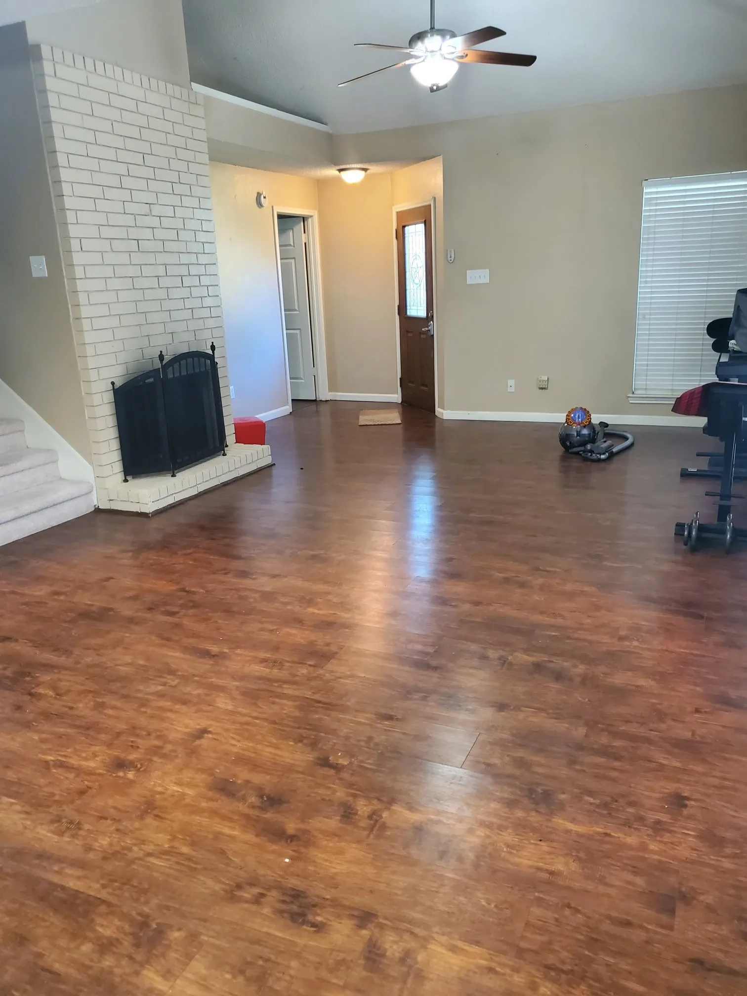 Spacious living area featuring wood-finish flooring, a white brick fireplace with a black metal screen, and a ceiling fan with integrated lighting