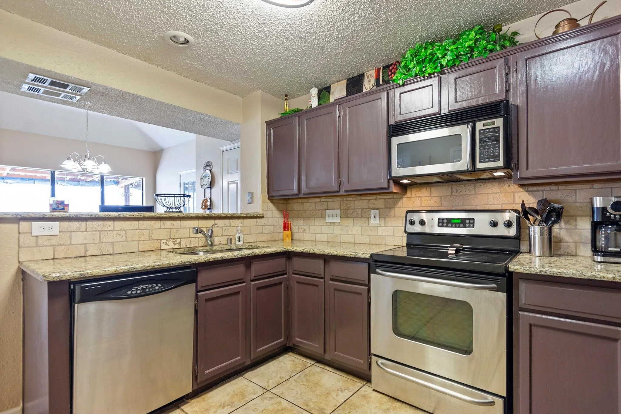 Kitchen featuring granite countertops, tile backsplash, stainless steel appliances, dark wood-finish cabinetry, and ceramic tile flooring