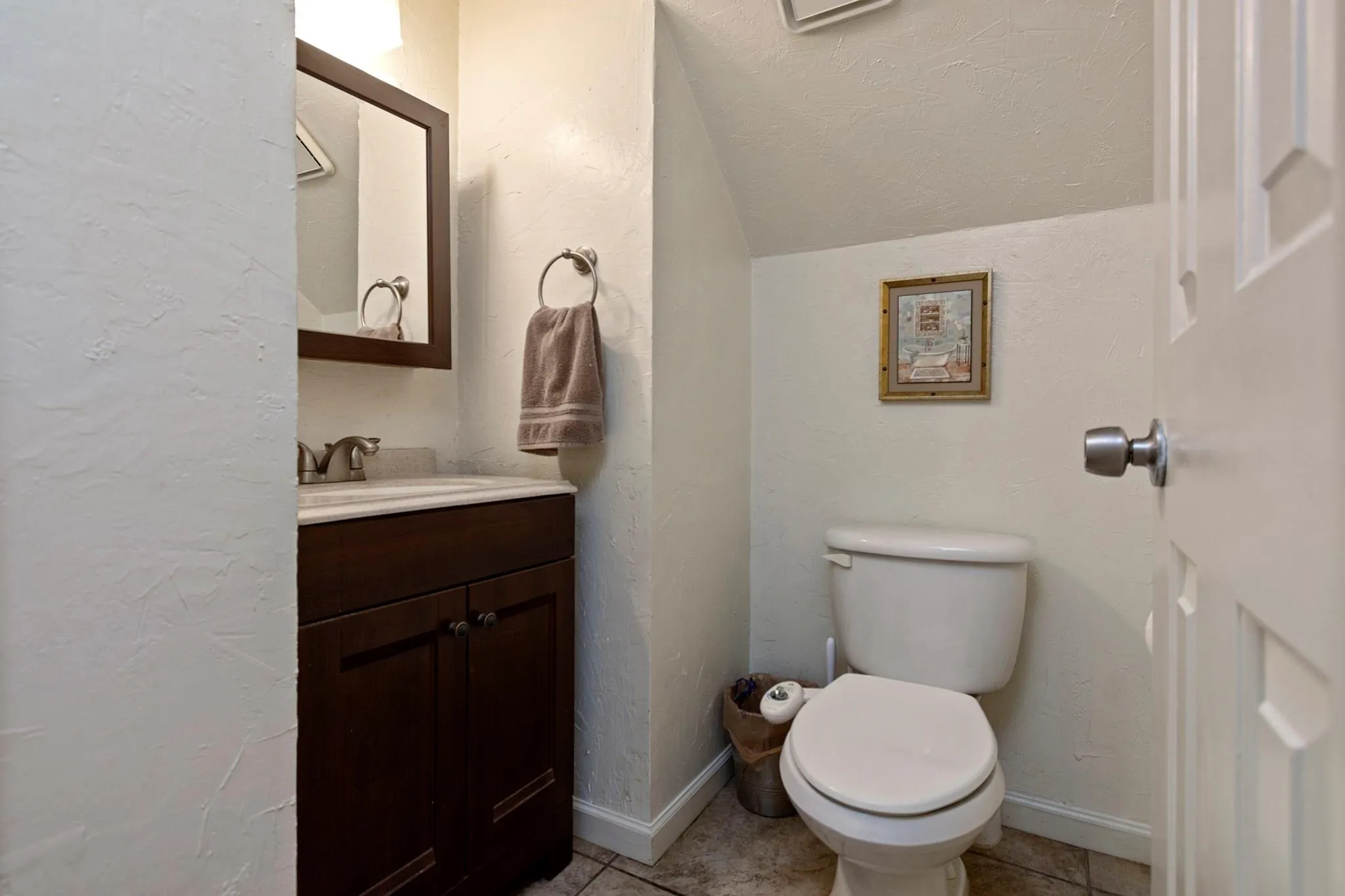 Powder room featuring a dark wood-finish vanity with a white countertop, coordinating framed mirror, and a white toilet