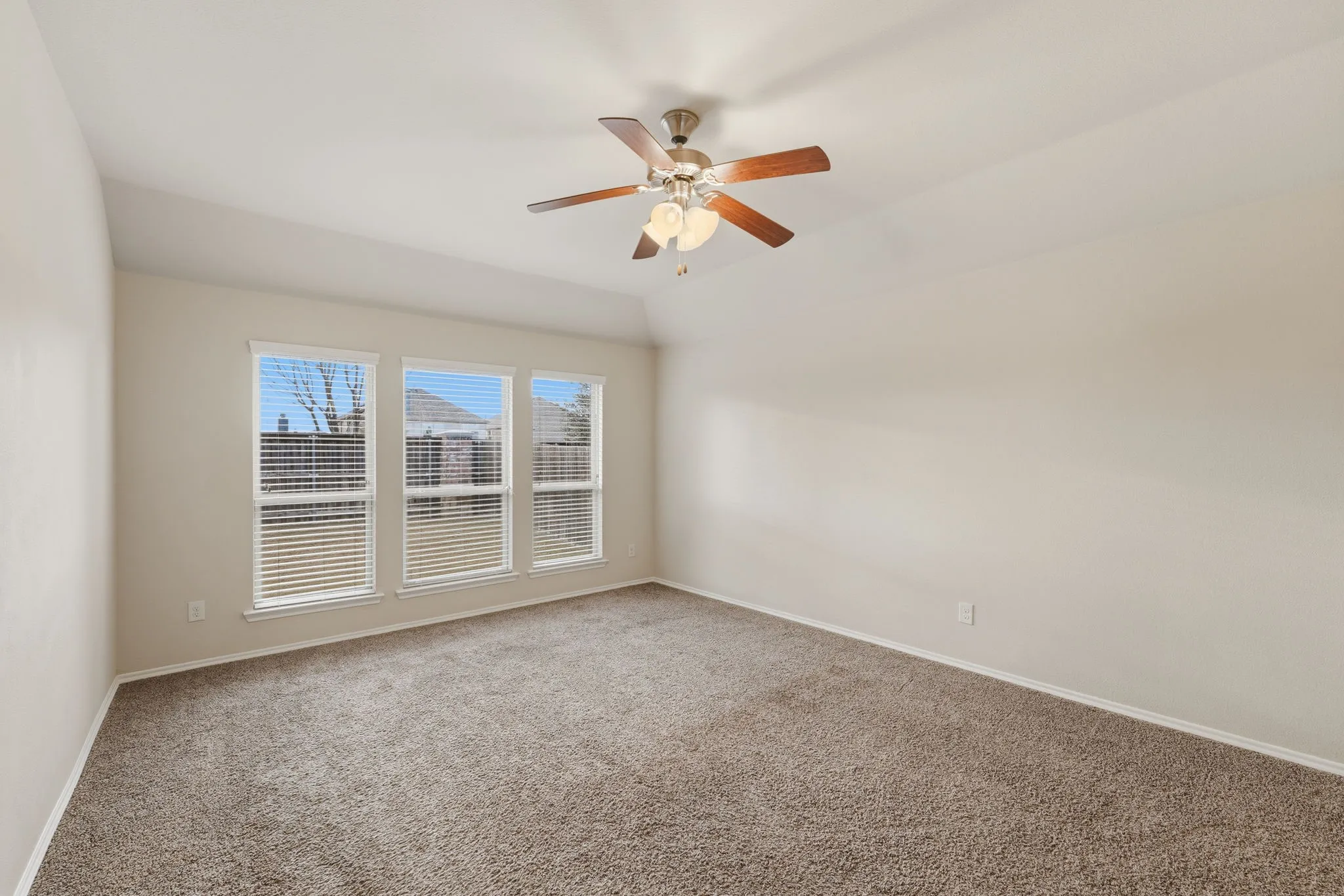 Carpeted room featuring three large windows with horizontal blinds, a vaulted ceiling, and a ceiling fan with integrated lighting