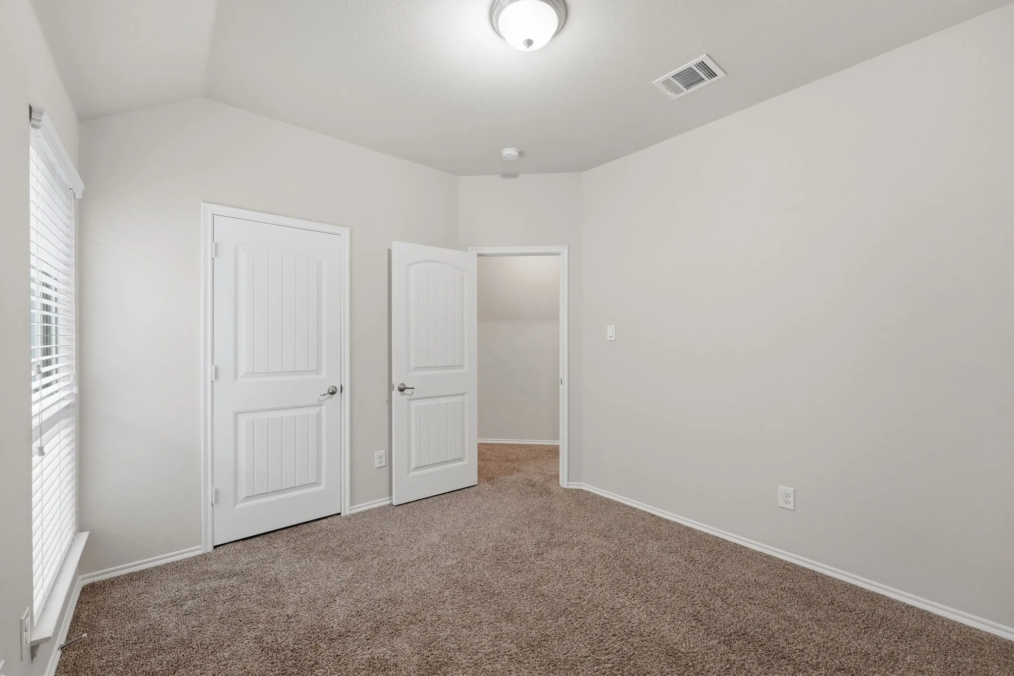 Carpeted room featuring a vaulted ceiling and a window with blinds