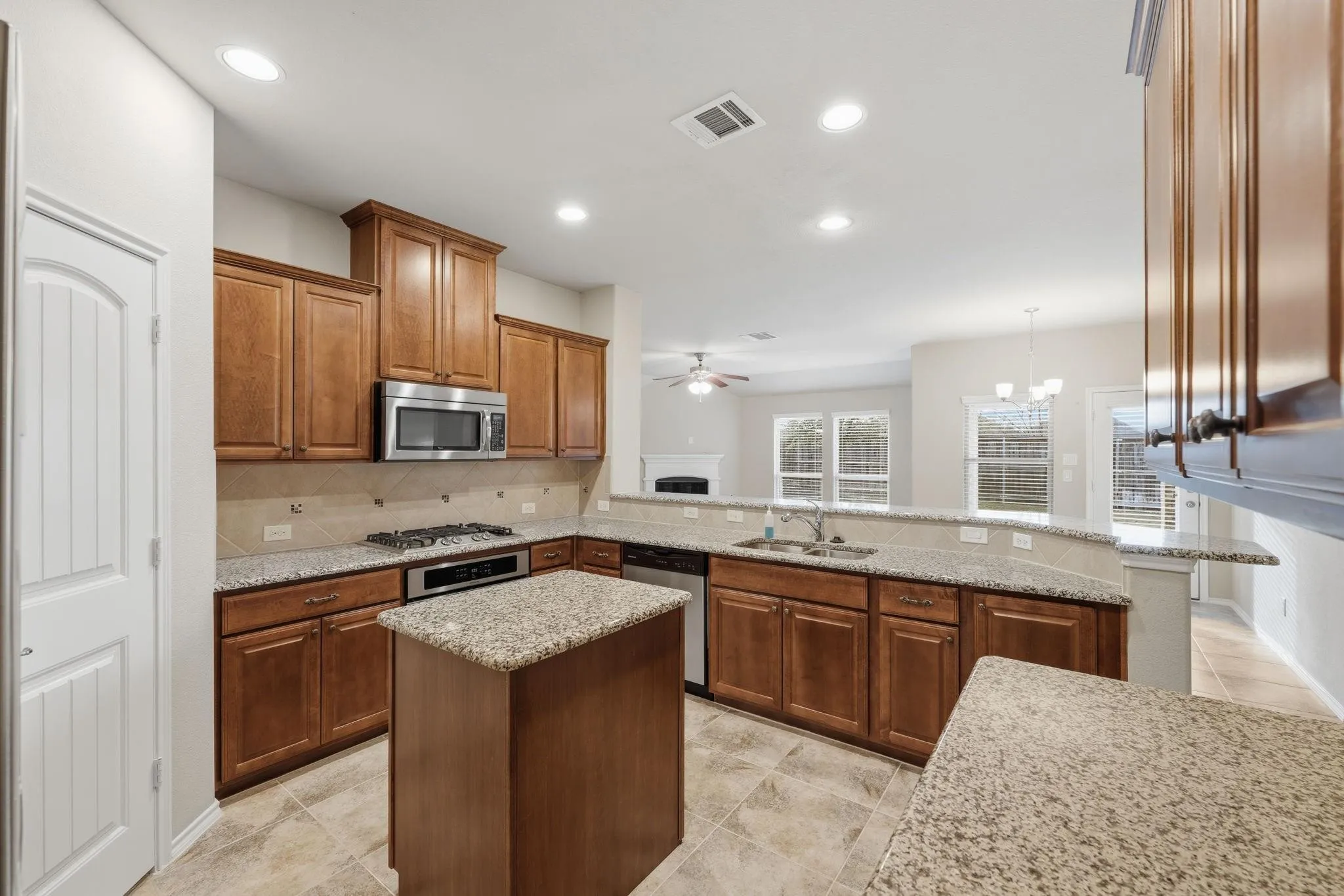 Expansive kitchen featuring granite countertops, wood-finish cabinetry, stainless steel appliances, a center island, and tile flooring
