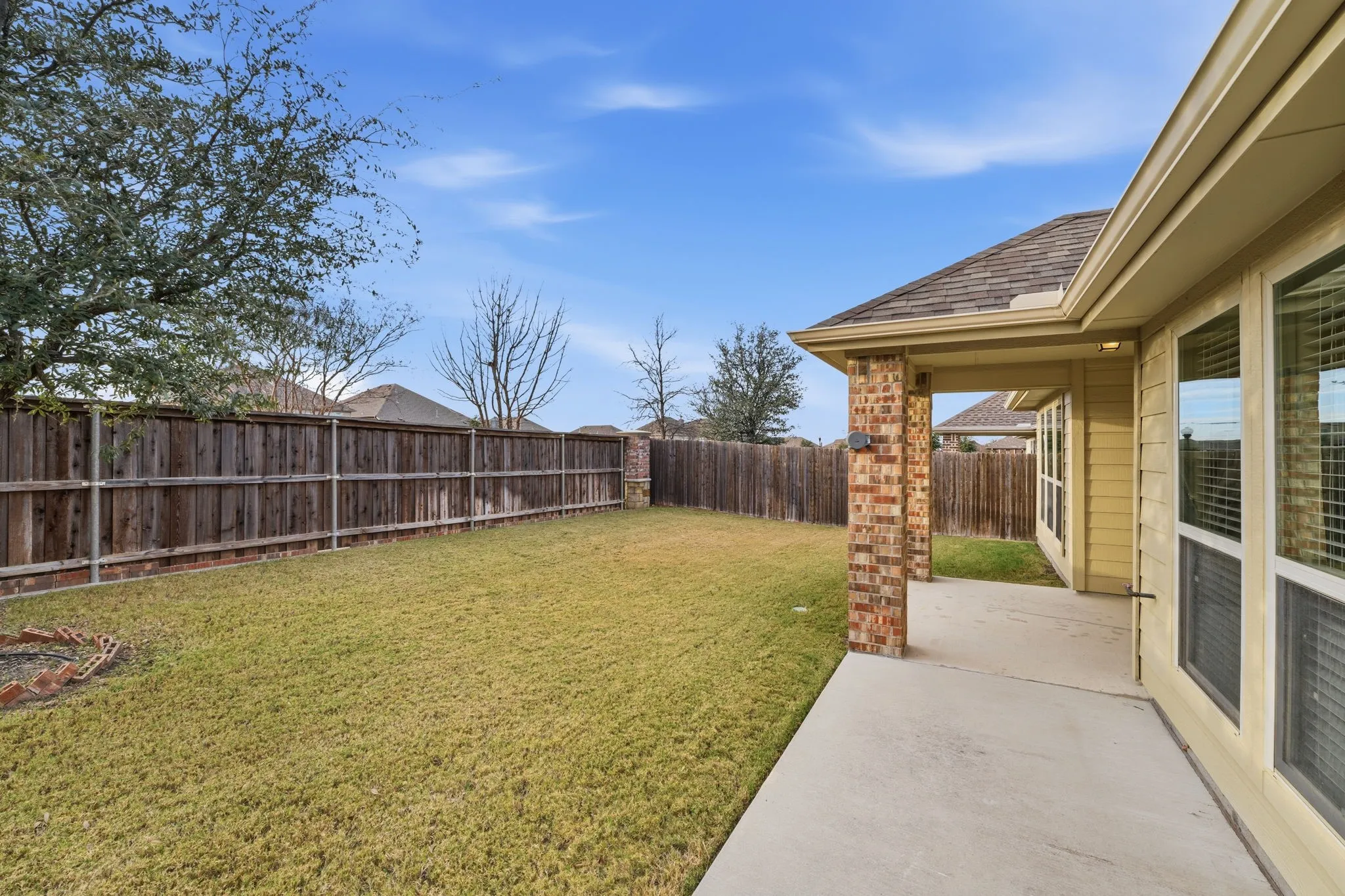 Expansive backyard featuring a covered patio with brick columns, a manicured lawn, and a privacy fence
