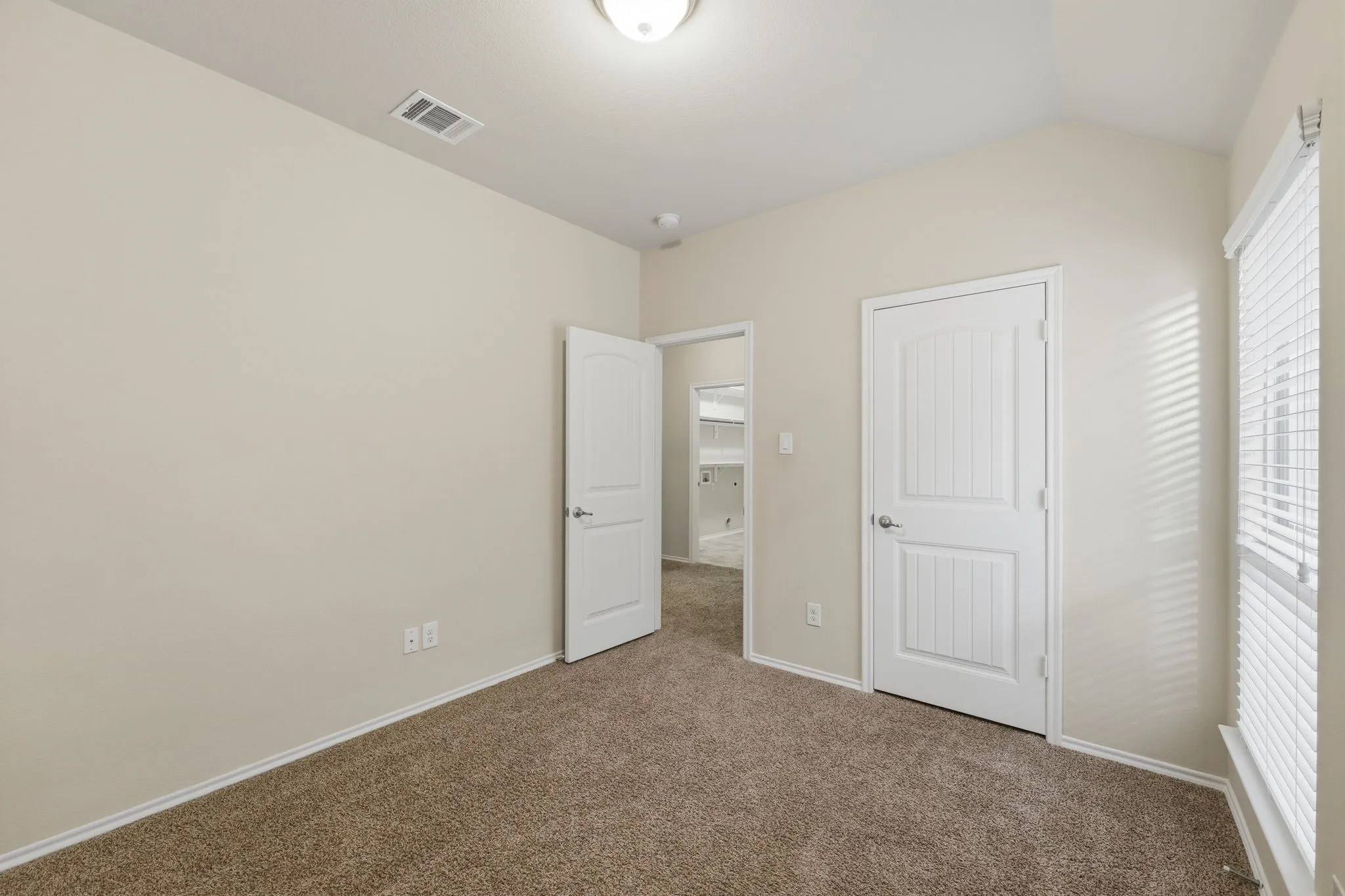 Carpeted interior room with vaulted ceilings and neutral wall tones