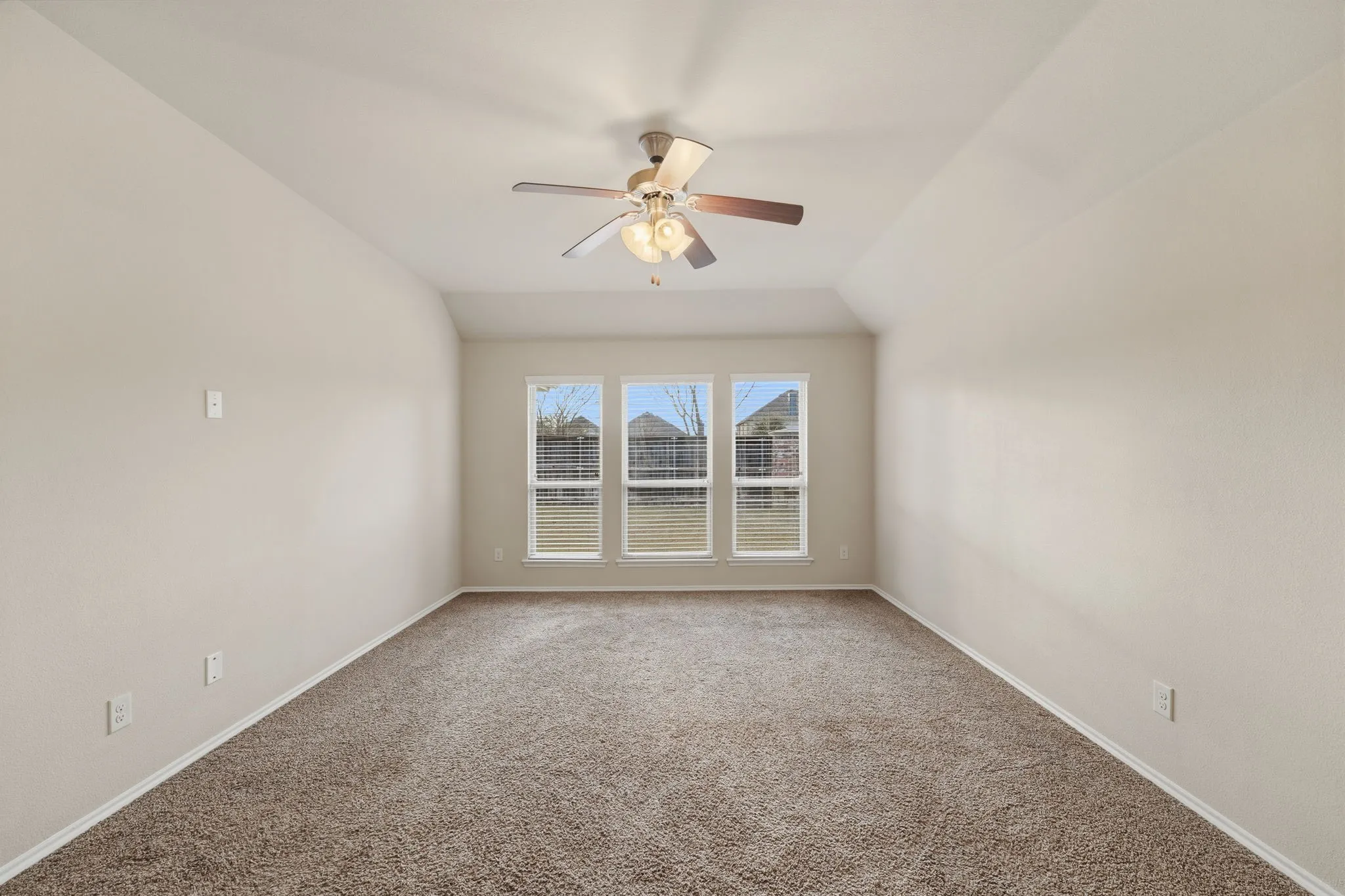 Spacious room featuring vaulted ceilings, neutral-toned carpeting, and a ceiling fan with light fixture