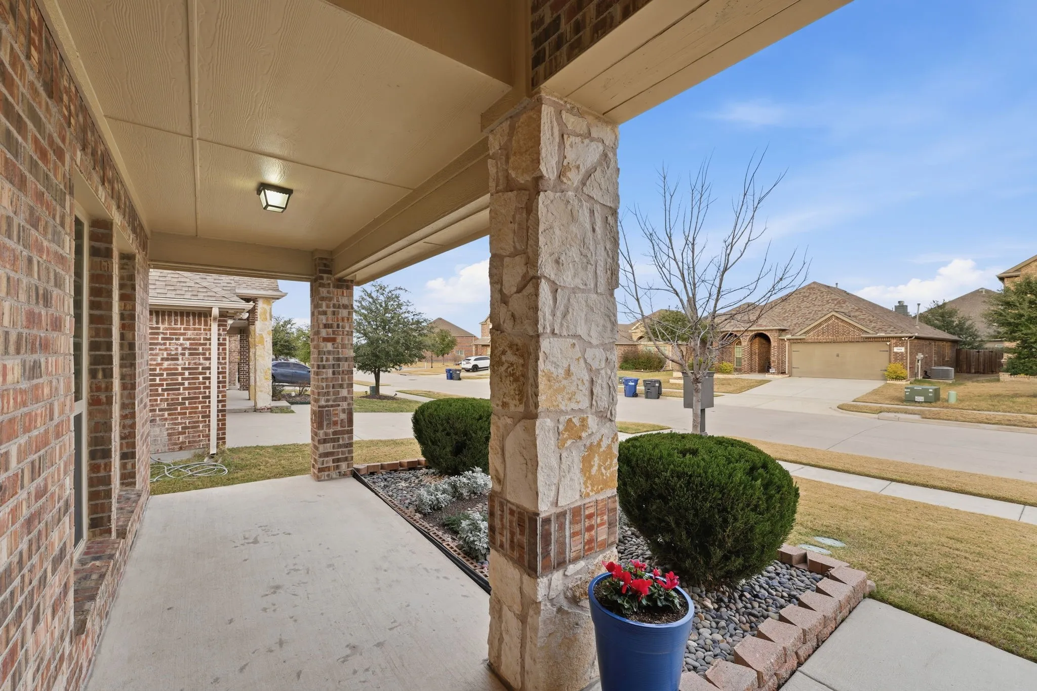 Covered front porch featuring a brick and stone facade, concrete flooring, and an overhead light fixture