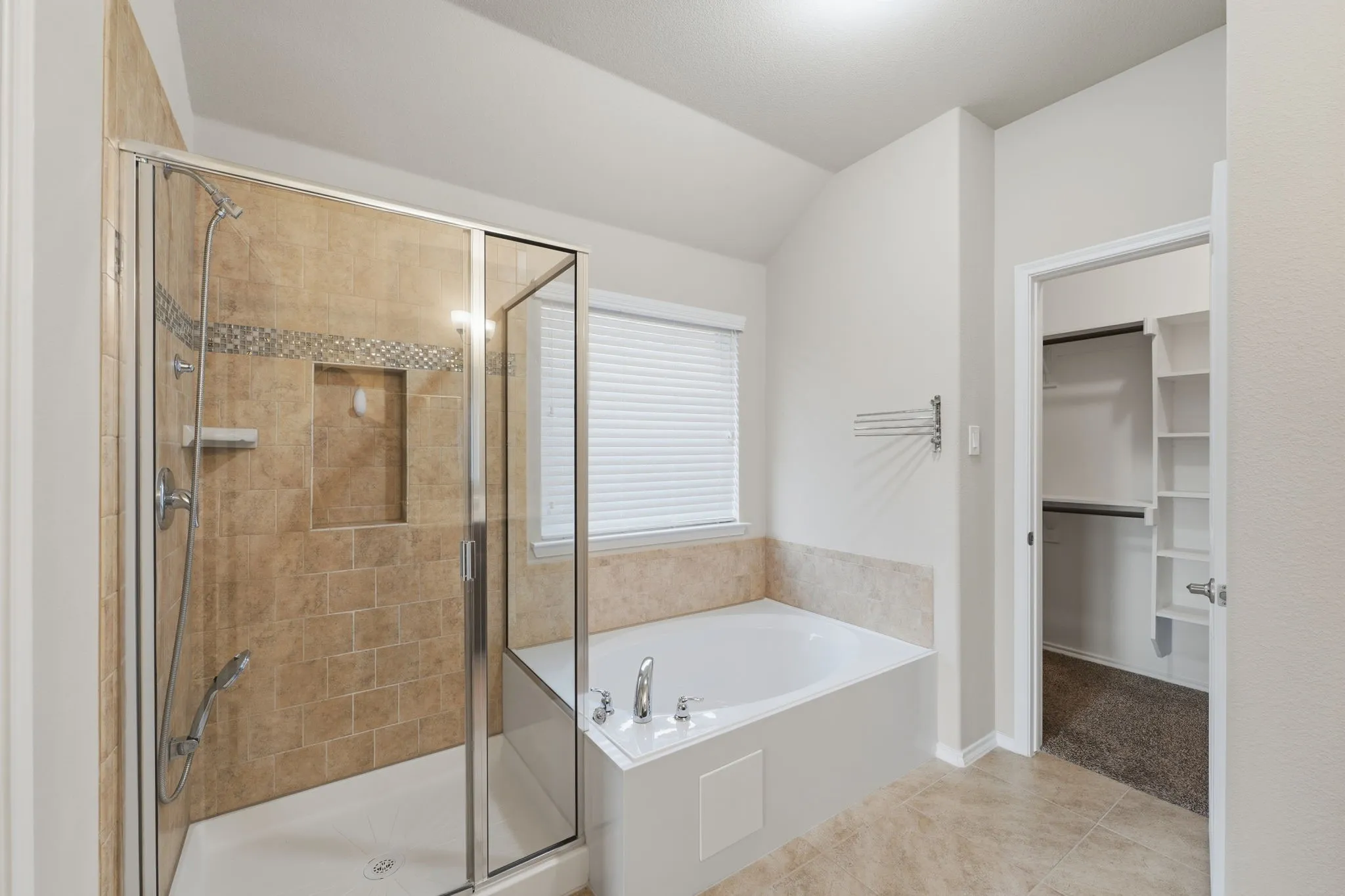 Bathroom featuring a tiled walk-in shower with glass enclosure, a built-in tub with window, and light-toned tile flooring