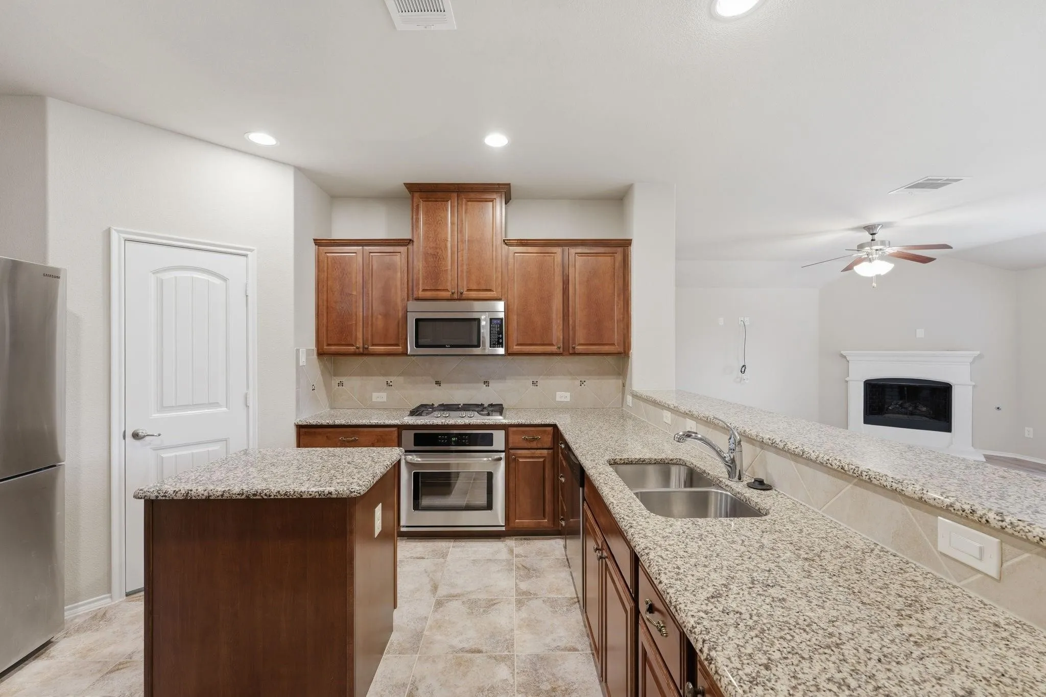 Open-concept kitchen featuring granite countertops, stainless steel appliances, wood cabinetry, and a double basin sink