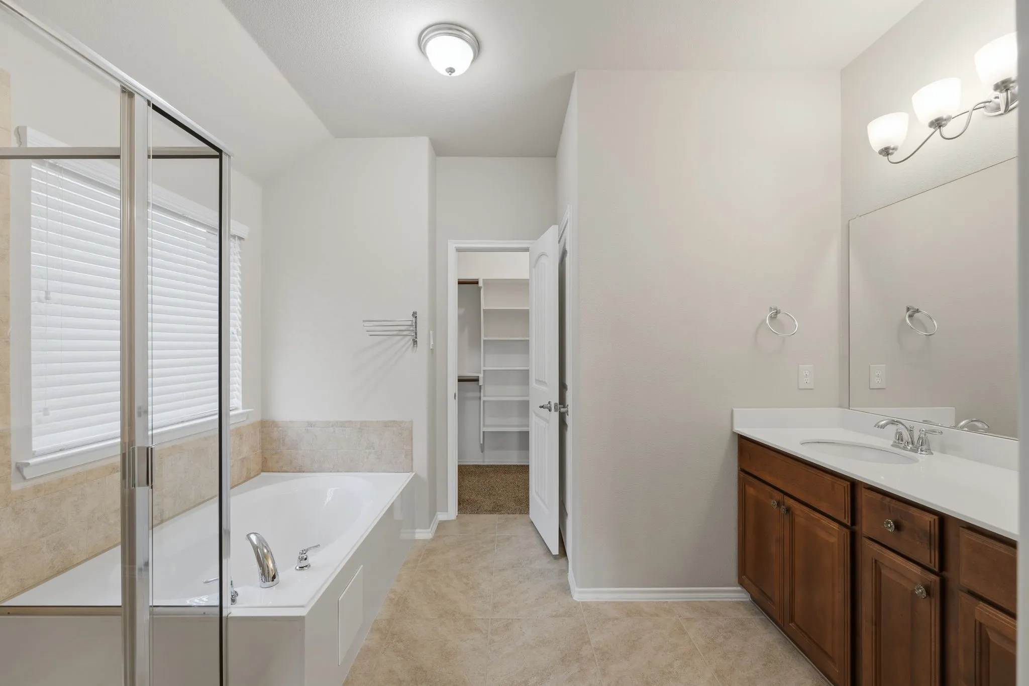 Bathroom featuring a built-in tub, separate glass-enclosed shower, a double vanity with a light-colored countertop, and a mirrored medicine cabinet