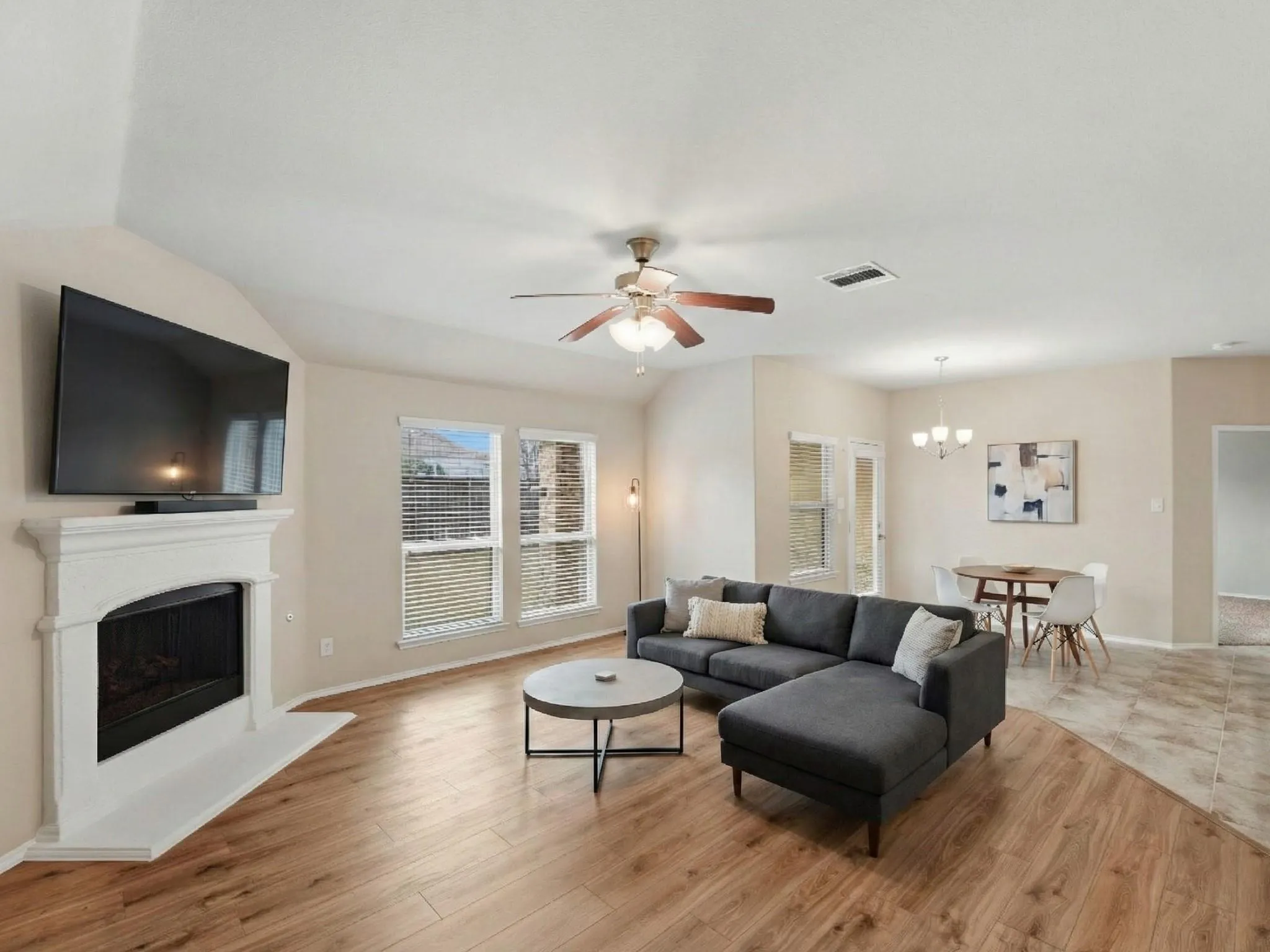 Living area featuring vaulted ceilings, wood-finish flooring, a white mantel fireplace, and a ceiling fan with integrated lighting