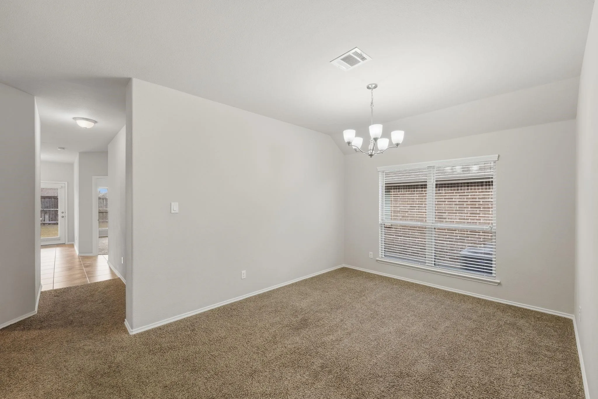 Carpeted room with a five-light chandelier, a window with blinds, and white trim