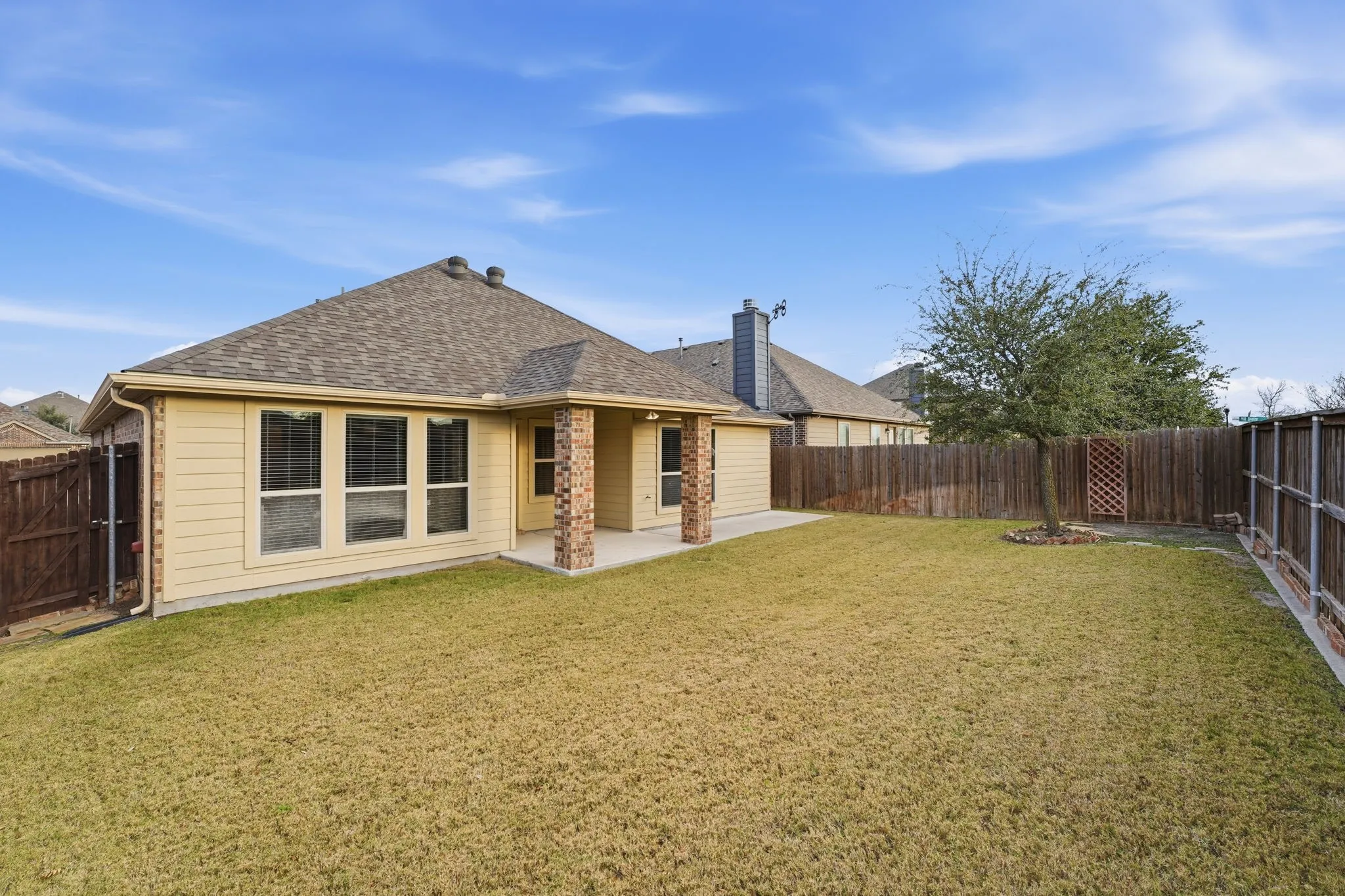 Spacious backyard featuring a covered patio with brick columns, a privacy fence, and a mature tree