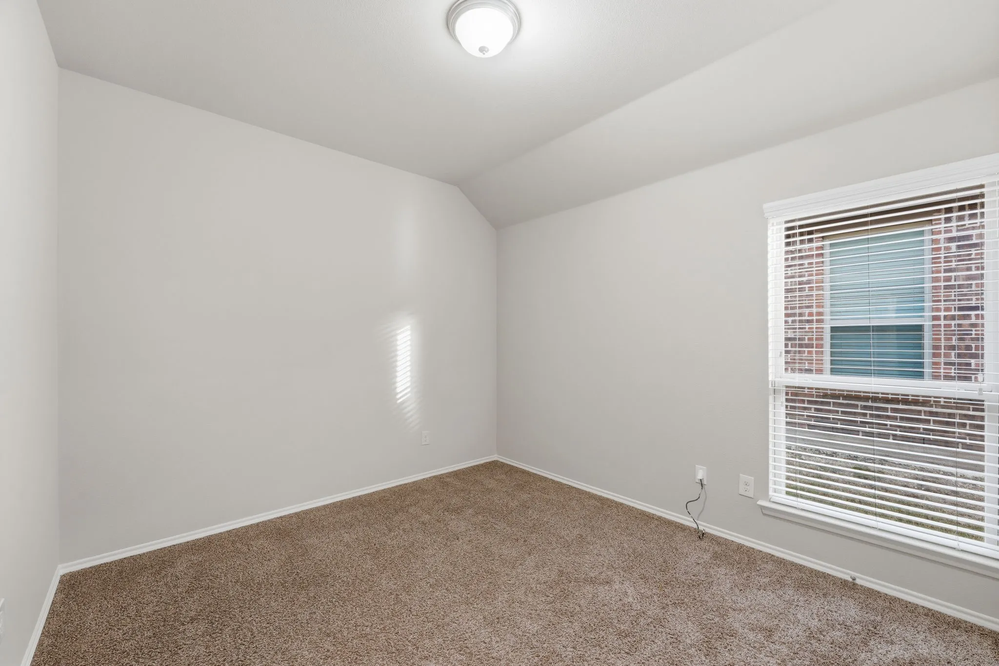 Neutral wall paint with textured carpet flooring, a window with blinds, and an overhead light fixture