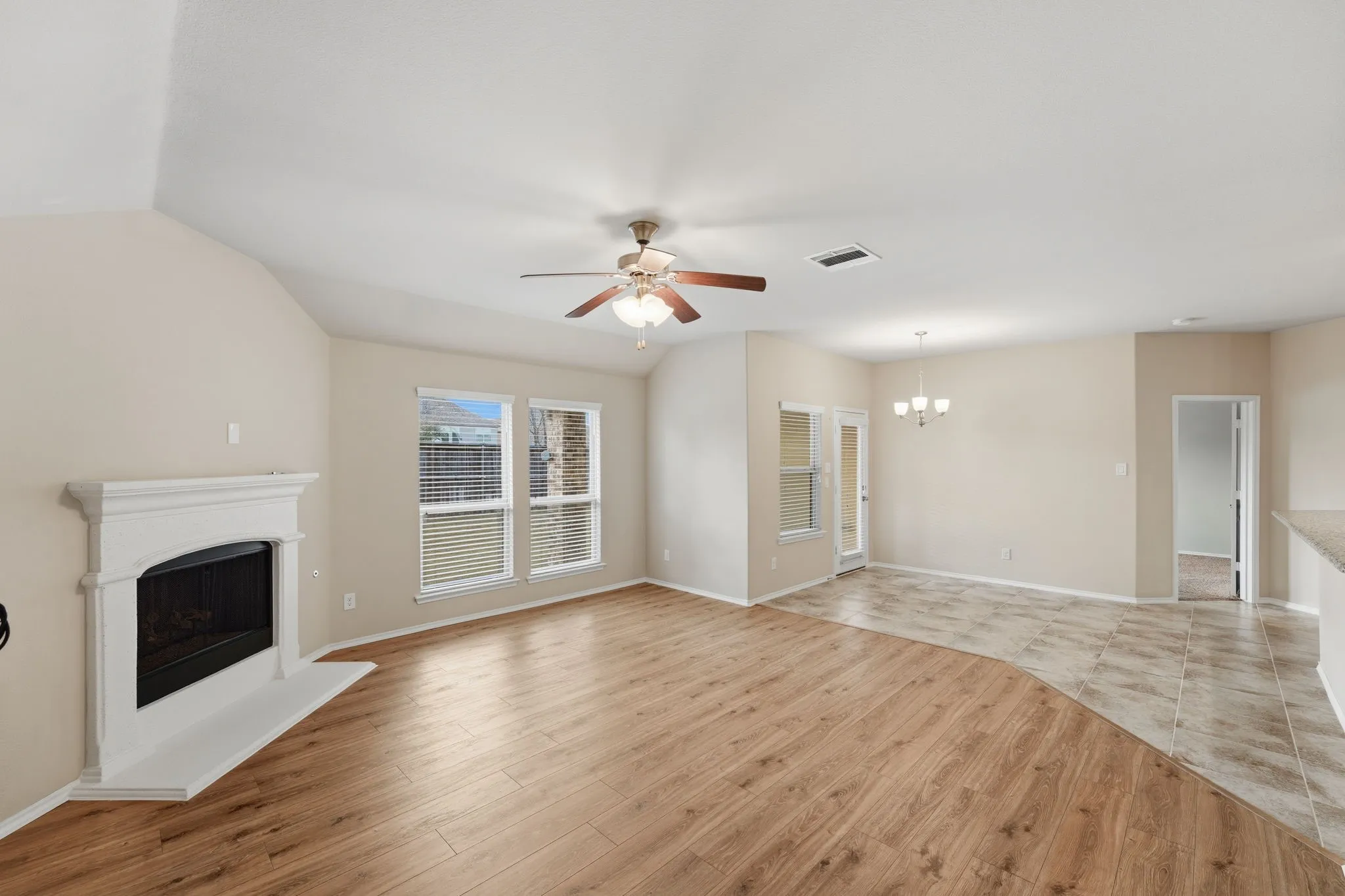 Spacious living area featuring a fireplace with a white mantel, wood-finish flooring, and vaulted ceilings