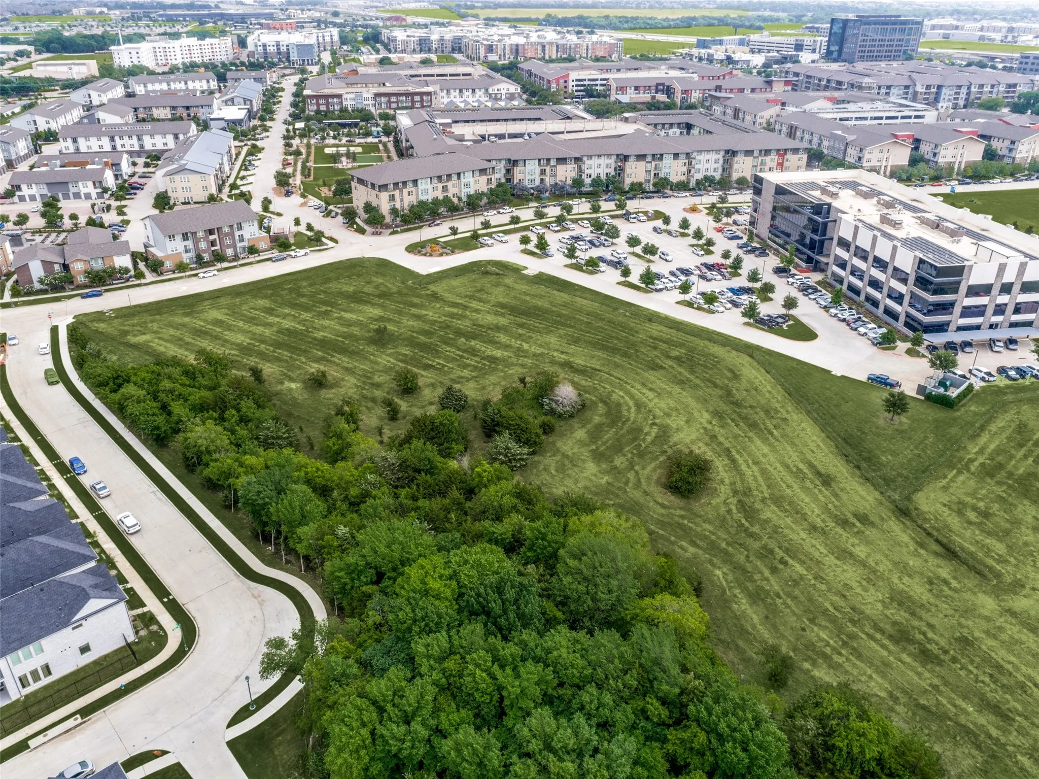 Expansive green space featuring natural vegetation and cleared areas, bordered by paved roads and sidewalks