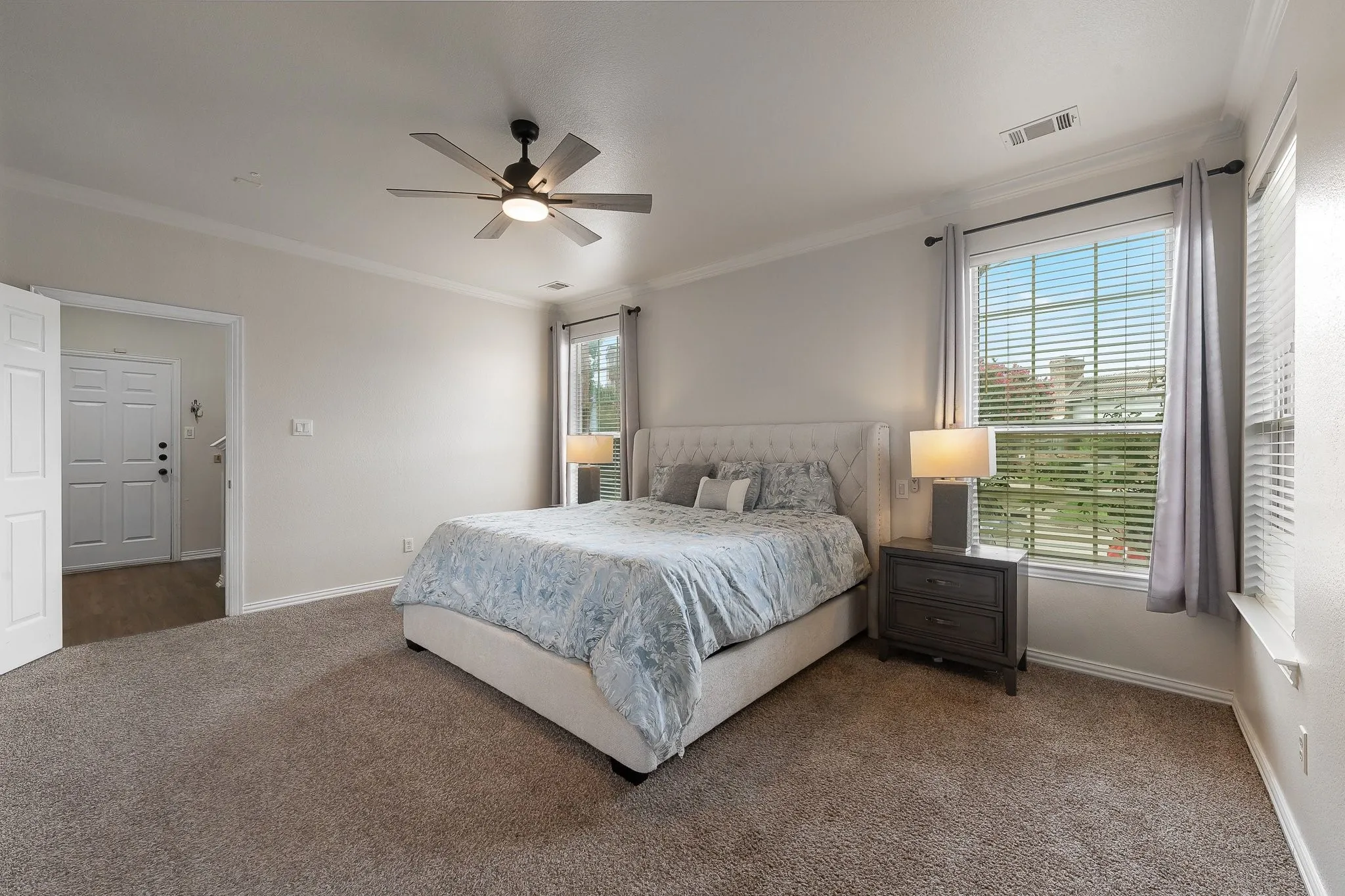 Carpeted bedroom featuring crown molding, a ceiling fan with integrated lighting, and two large windows with blinds and curtain rods