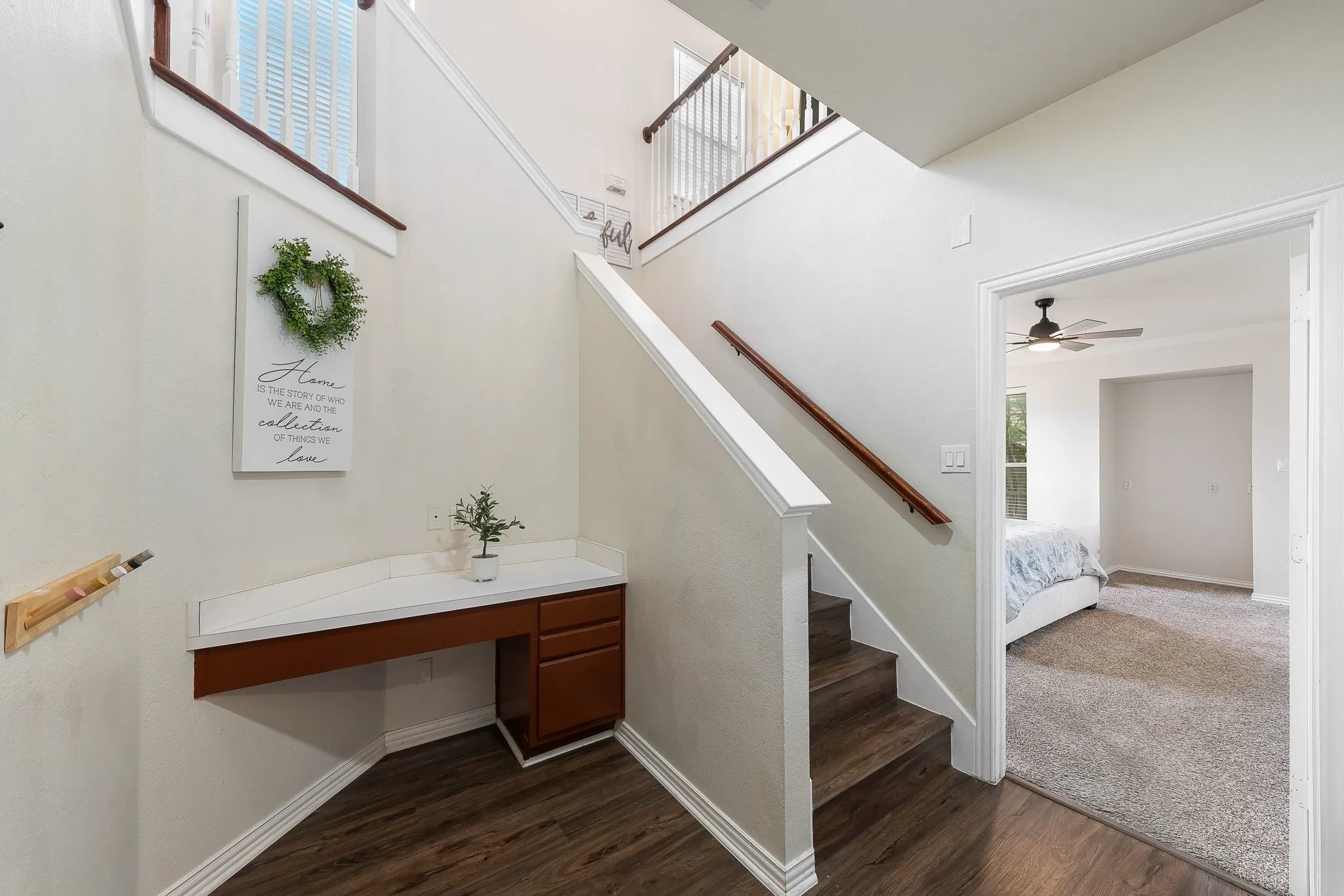 Staircase with wood-finish treads and handrail, featuring a built-in desk with a light-colored countertop and wood-finish cabinetry