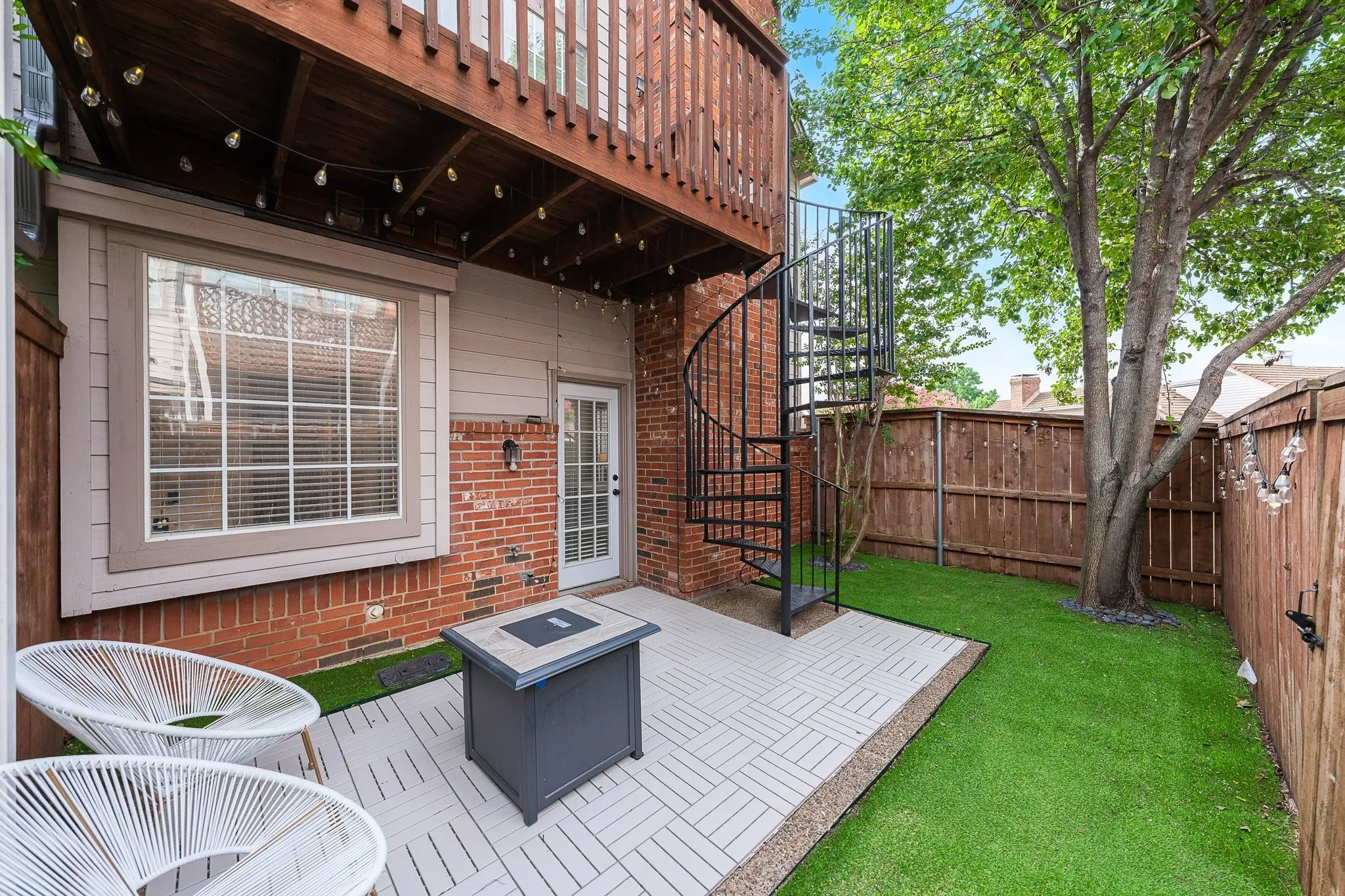 Backyard patio featuring a black spiral staircase, wood privacy fencing, and a manicured lawn