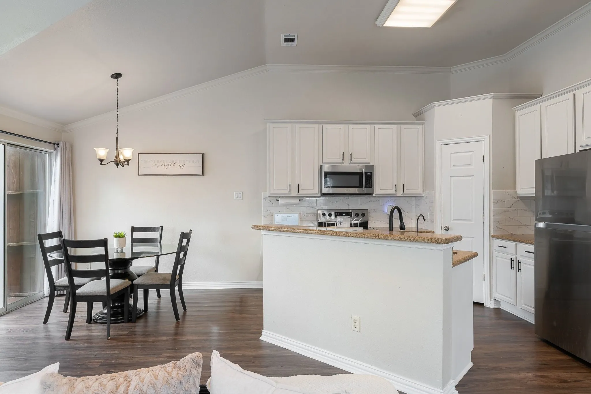 Open-concept kitchen and dining area featuring wood-finish flooring, white cabinetry, stainless steel appliances, and a breakfast bar