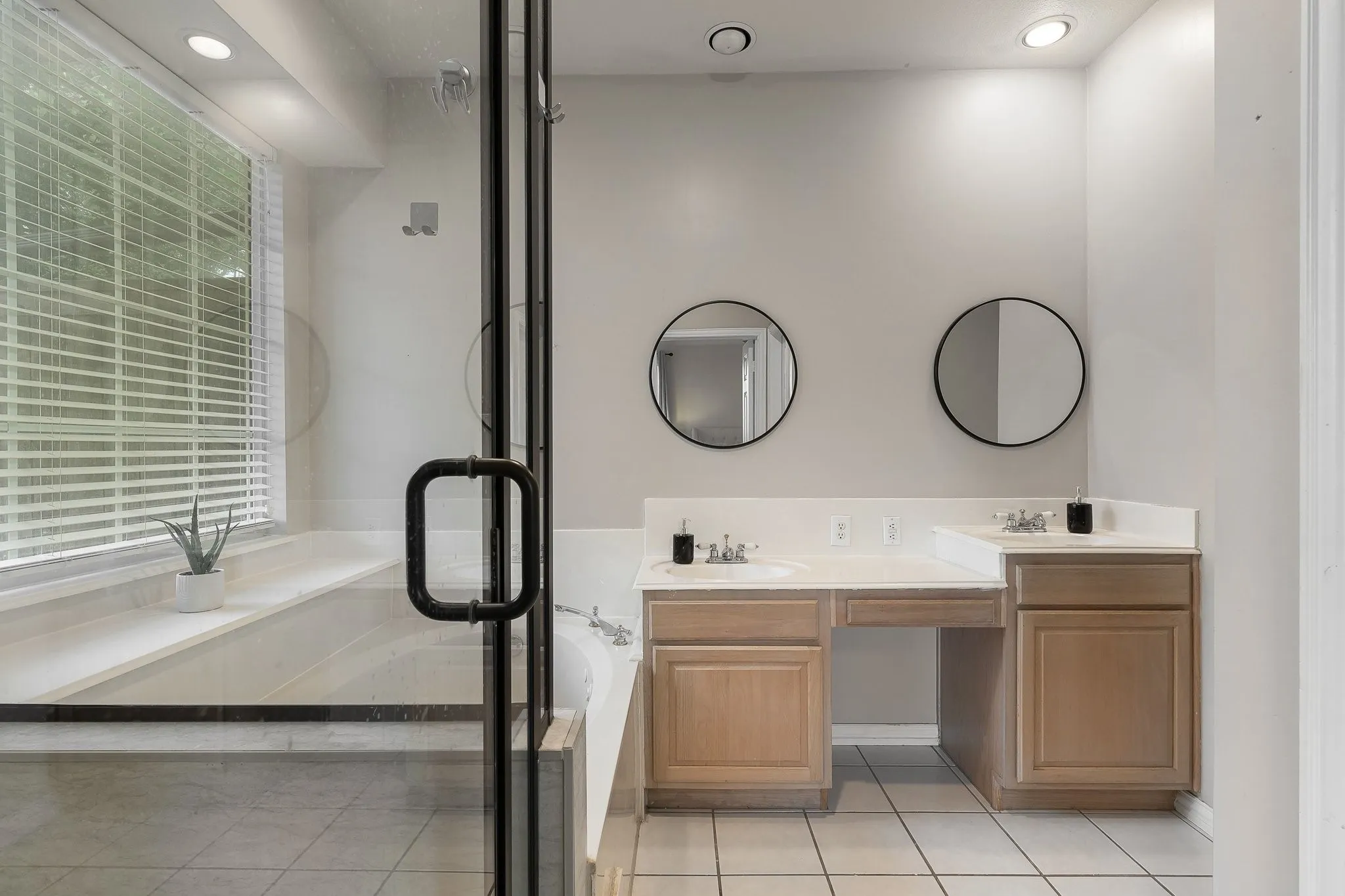 Bathroom featuring a glass-enclosed shower, built-in soaking tub, dual vanities with integrated sinks, wood cabinetry, and tiled flooring