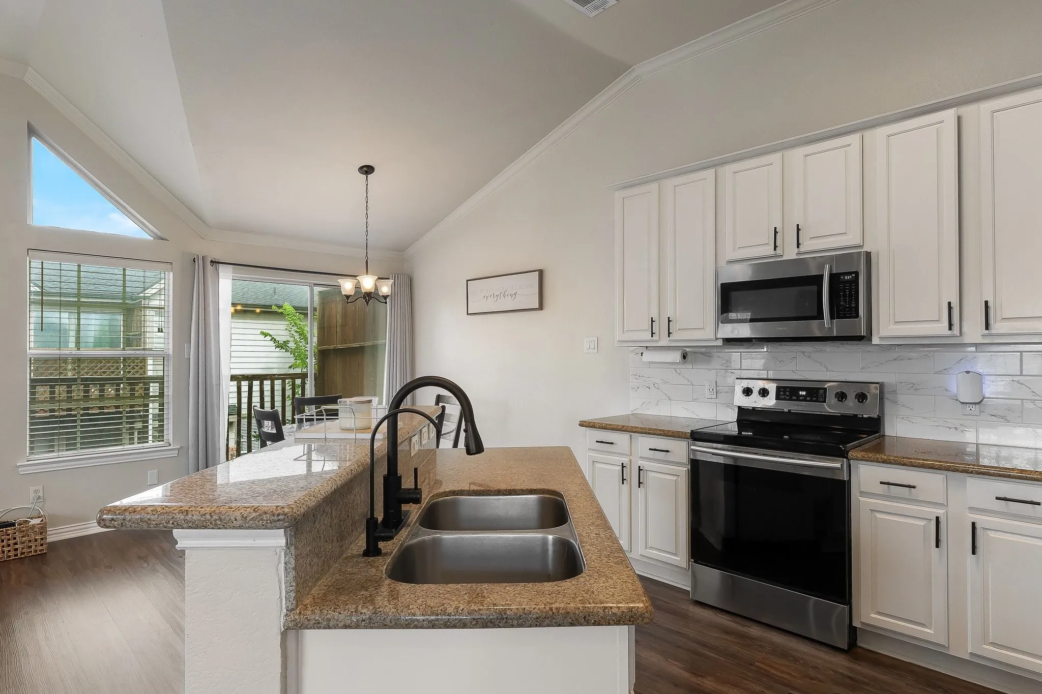 Kitchen featuring a dual basin sink with a matte black high-arc faucet, granite countertops, and white shaker-style cabinetry with matte black hardware