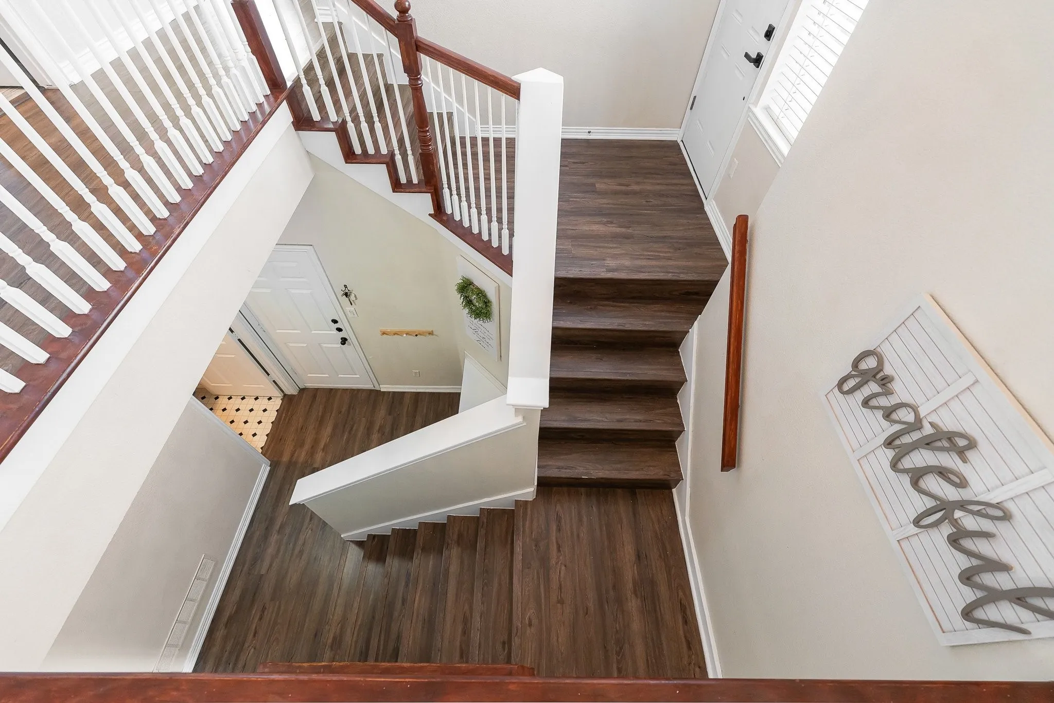 Multi-level interior featuring wood-finish flooring throughout, white painted walls, and a staircase with dark wood handrails and white balusters