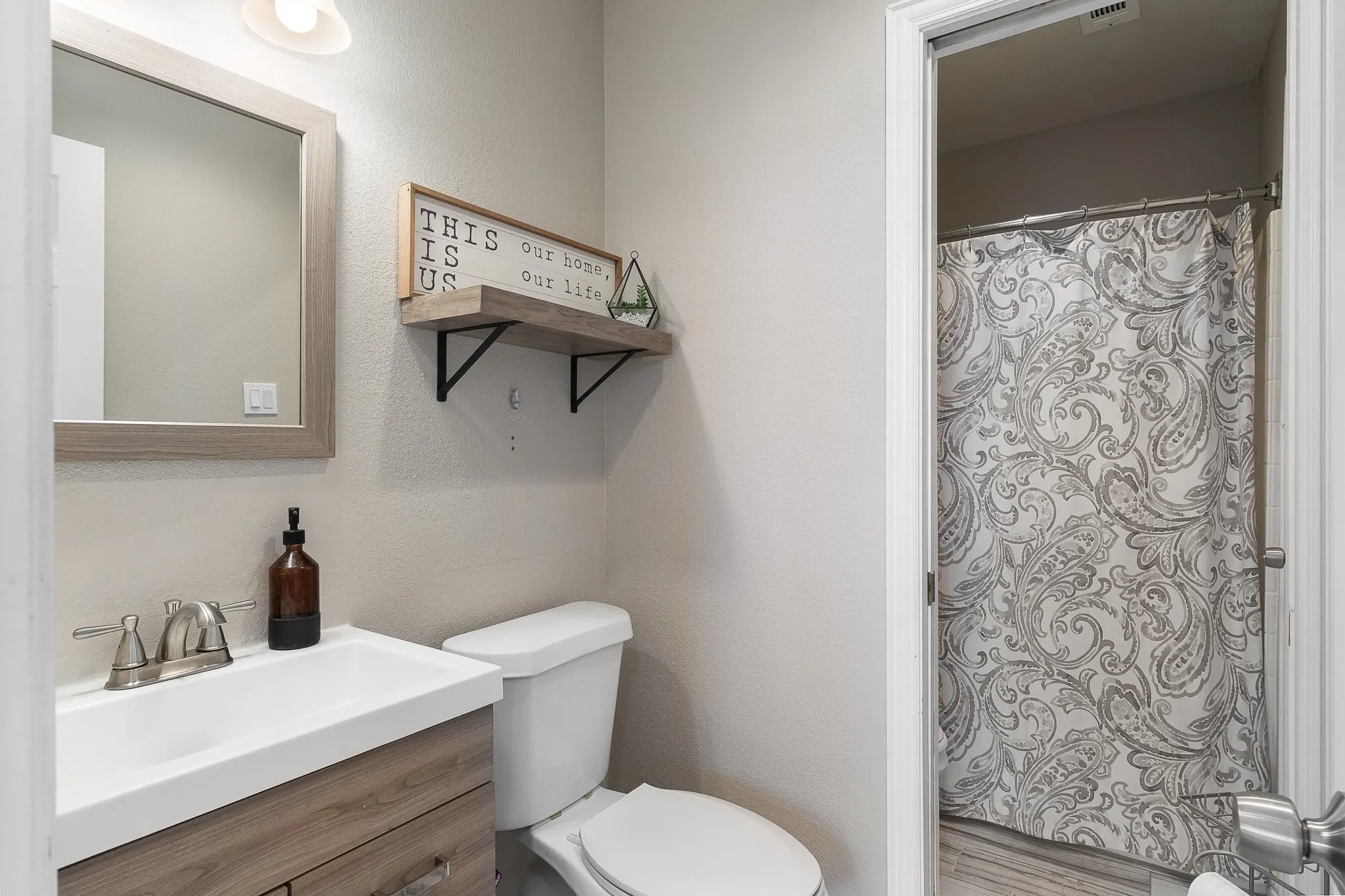 Bathroom featuring a wood-finish vanity with an integrated sink and brushed nickel faucet, a framed mirror, and a white toilet