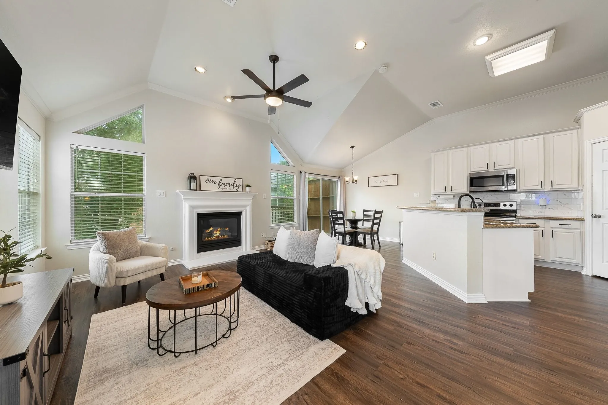 Open-concept living space featuring vaulted ceilings, a built-in fireplace with a mantel, and wood-finish flooring