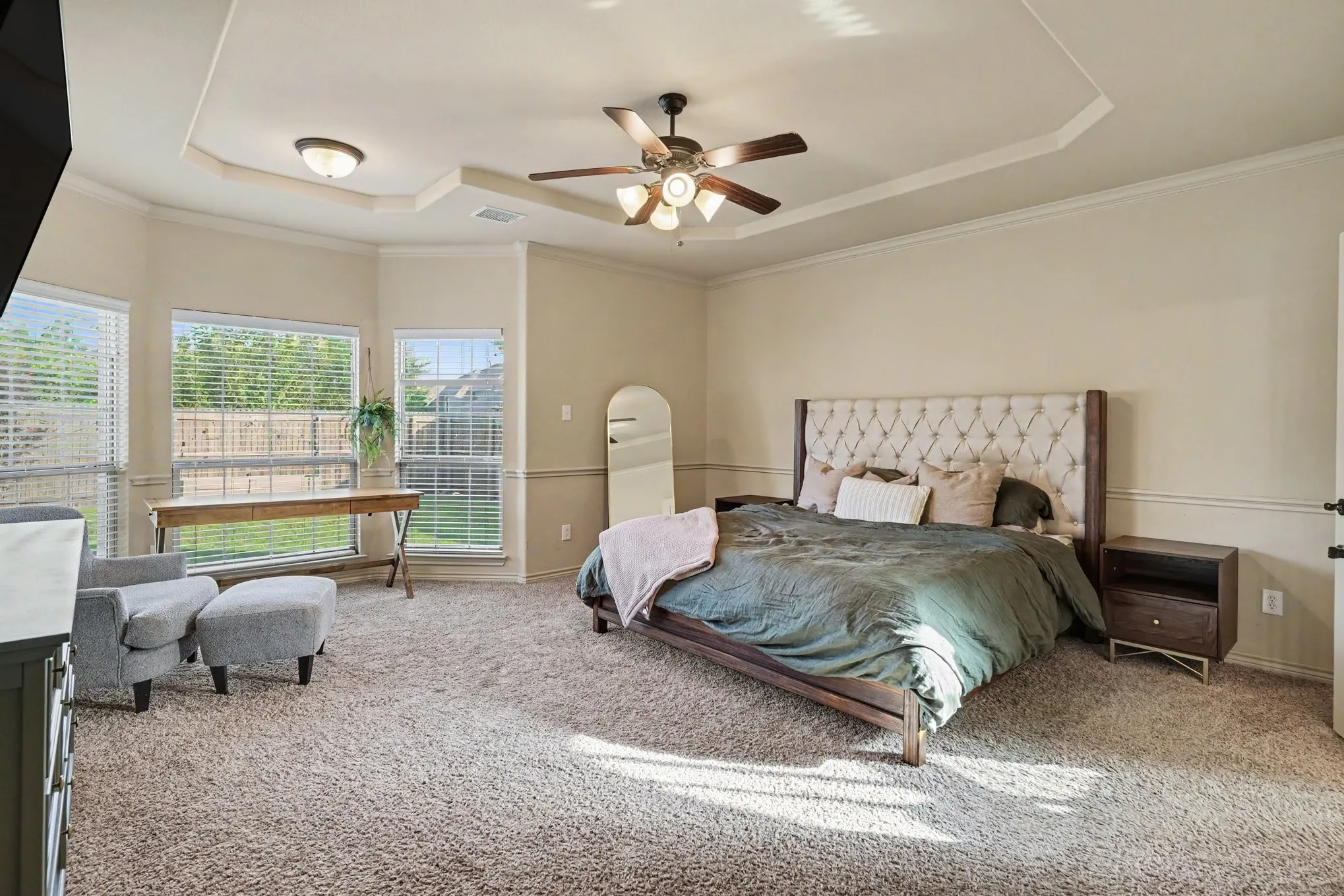 Spacious carpeted room featuring a ceiling fan with integrated lighting, a tray ceiling, and crown molding