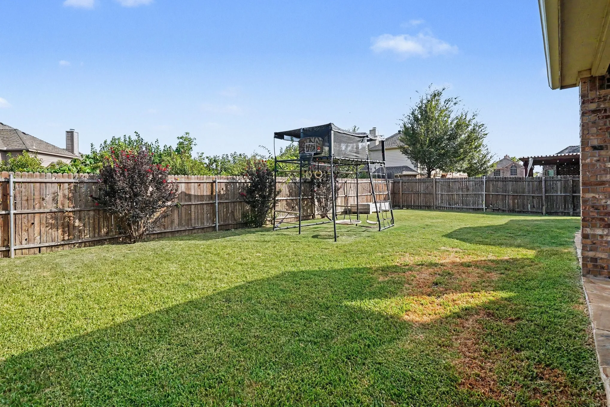 Expansive grassy backyard featuring a full privacy fence, mature trees, and landscaping elements