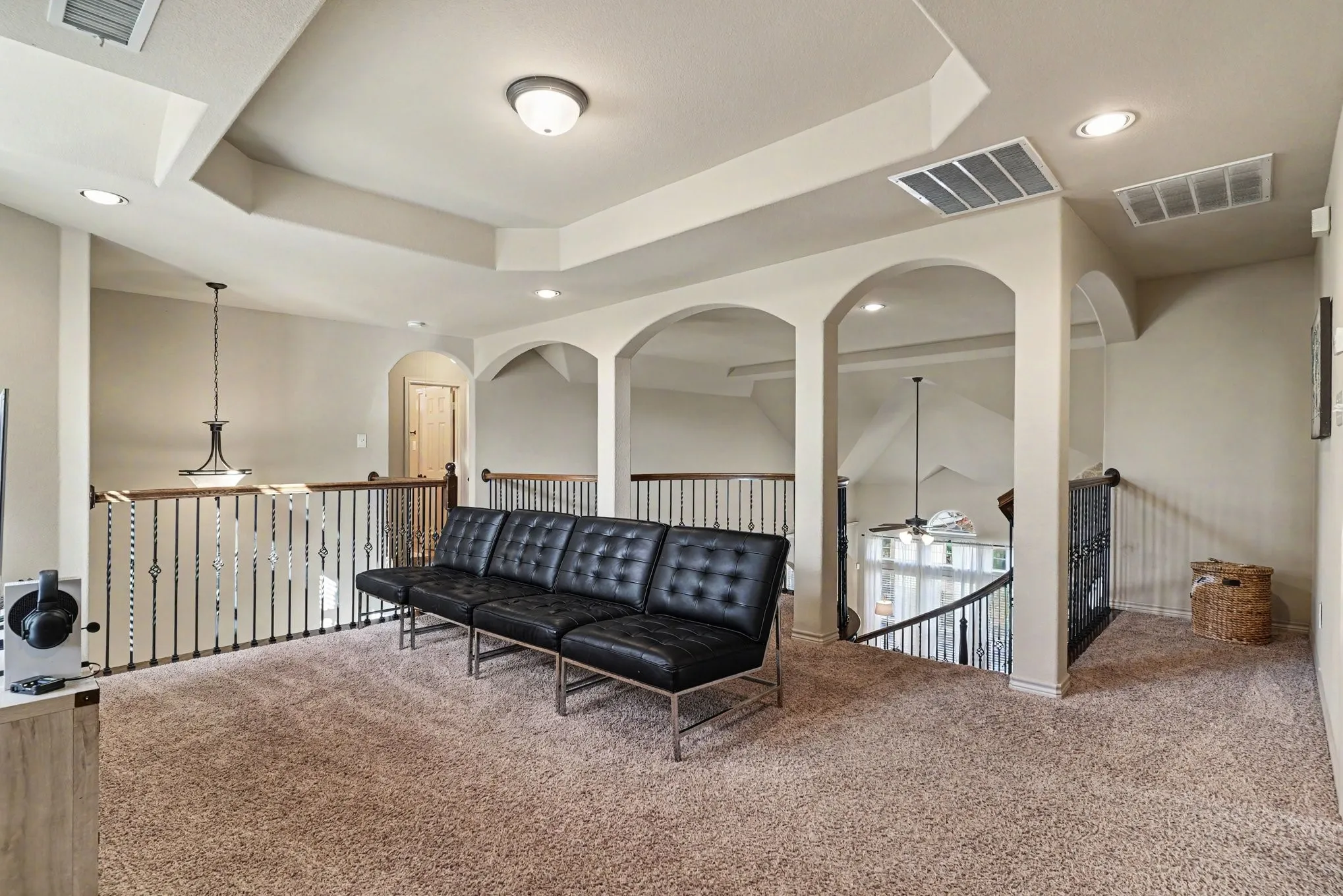 Spacious loft area featuring tray ceilings, recessed lighting, arched doorways, and light brown carpeting