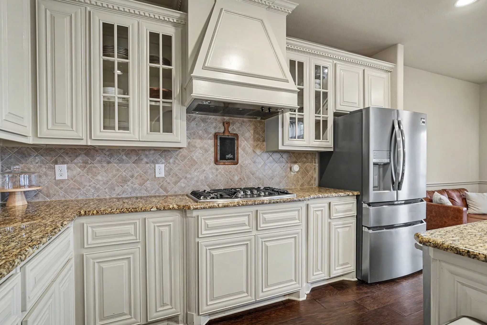 Kitchen featuring light-colored cabinetry with glass-front accents, granite countertops, a diamond-patterned tile backsplash, a built-in range, and dark wood-finish flooring
