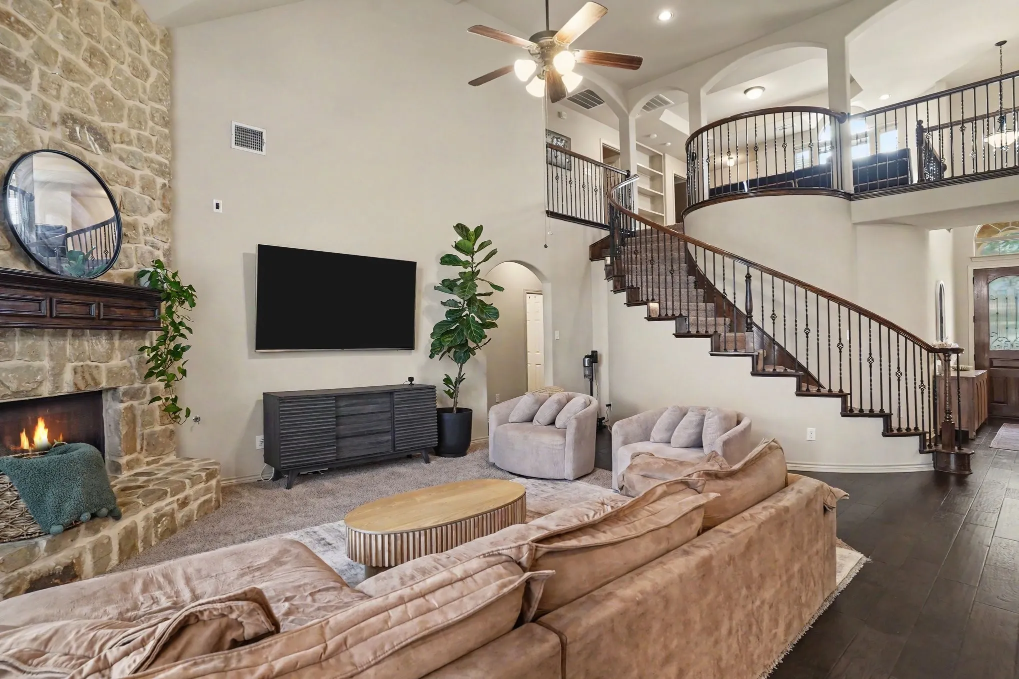 Living area featuring a stone-clad fireplace with a wood mantel, high ceilings with a ceiling fan, and a curved staircase with dark wood treads and wrought iron balusters