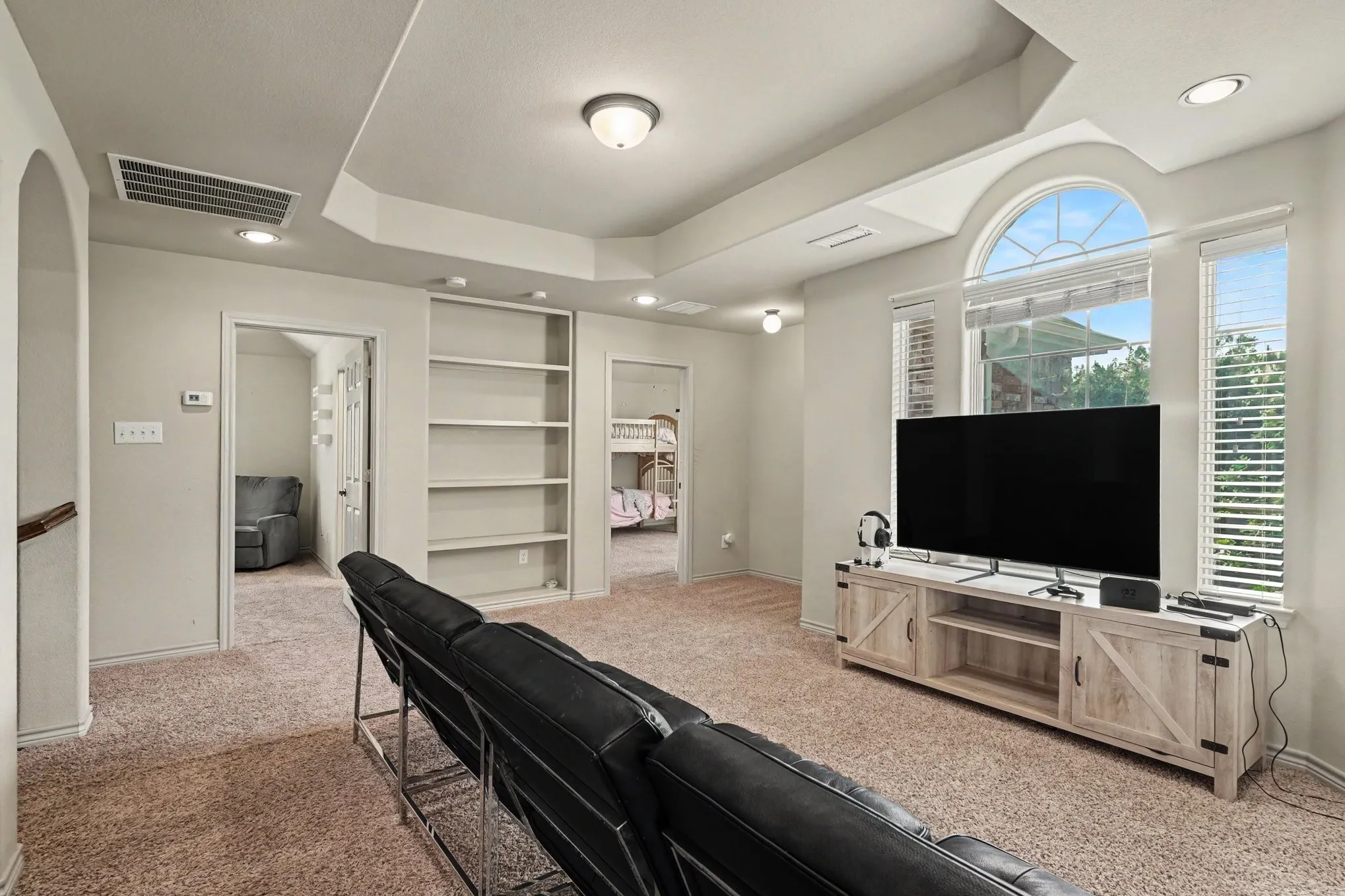 Spacious bonus room featuring an arched picture window, recessed lighting, built-in shelving, and tray ceiling details